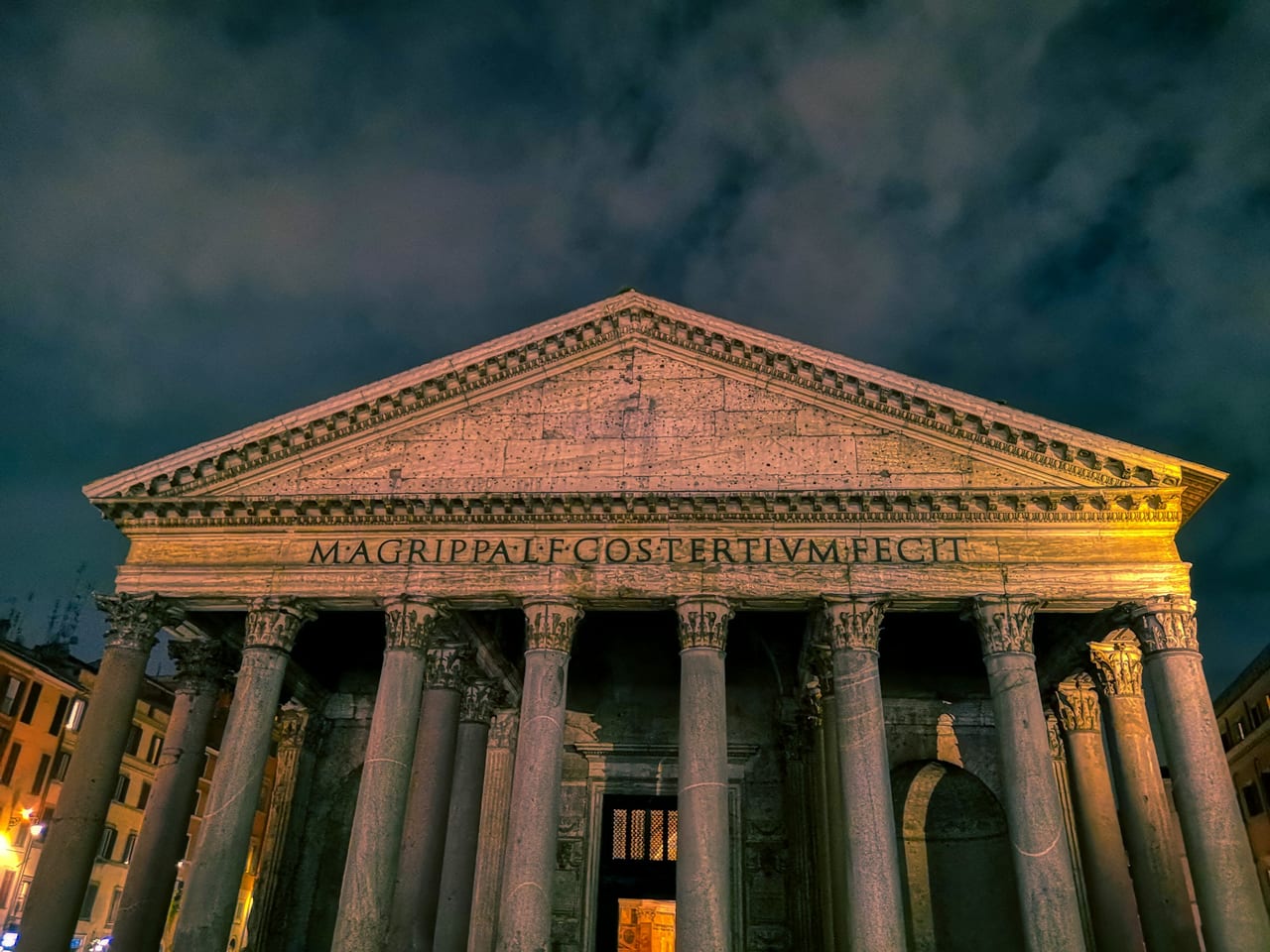 The Pantheon's granite columns and inscribed portico stand lit at dusk in Piazza della Rotonda.