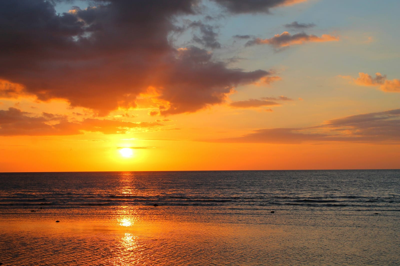 The sun rises over a calm ocean, casting a bright orange reflection across the water.