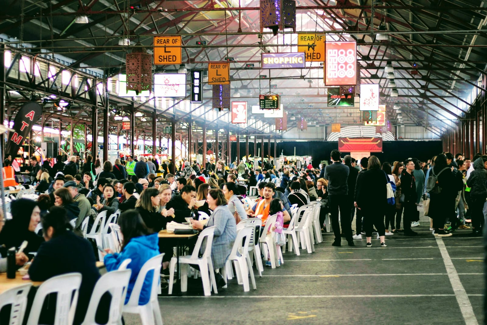 A bustling food hall with diners at communal tables and vendors in the background.