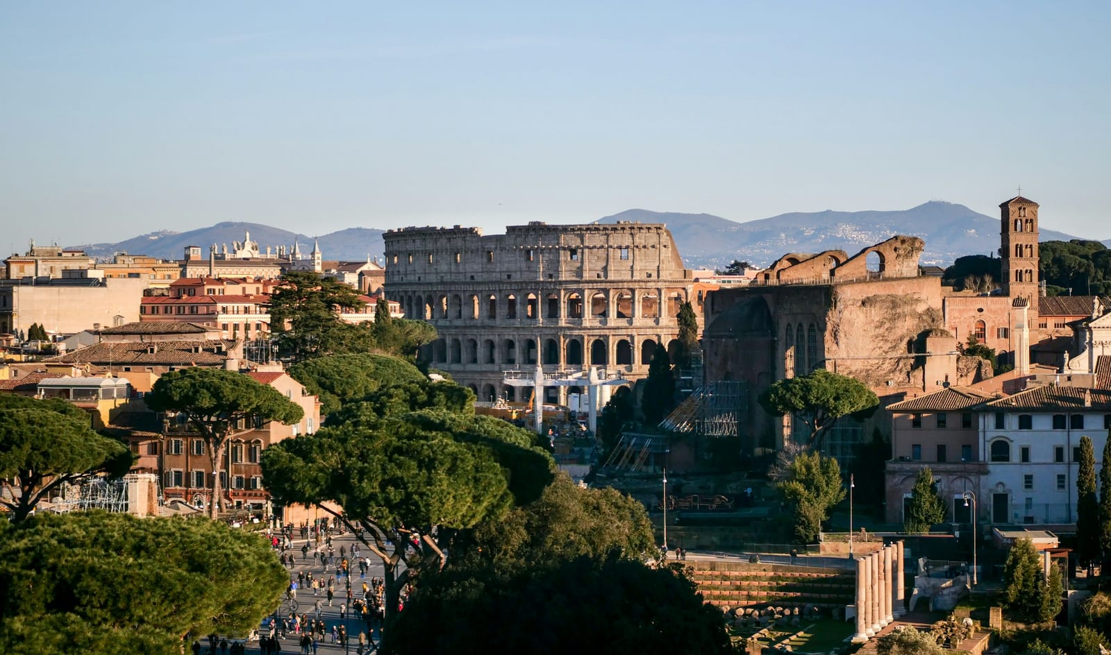 The Colosseum rising above the rooftops and umbrella pines of central Rome, with the Alban Hills in the distance.