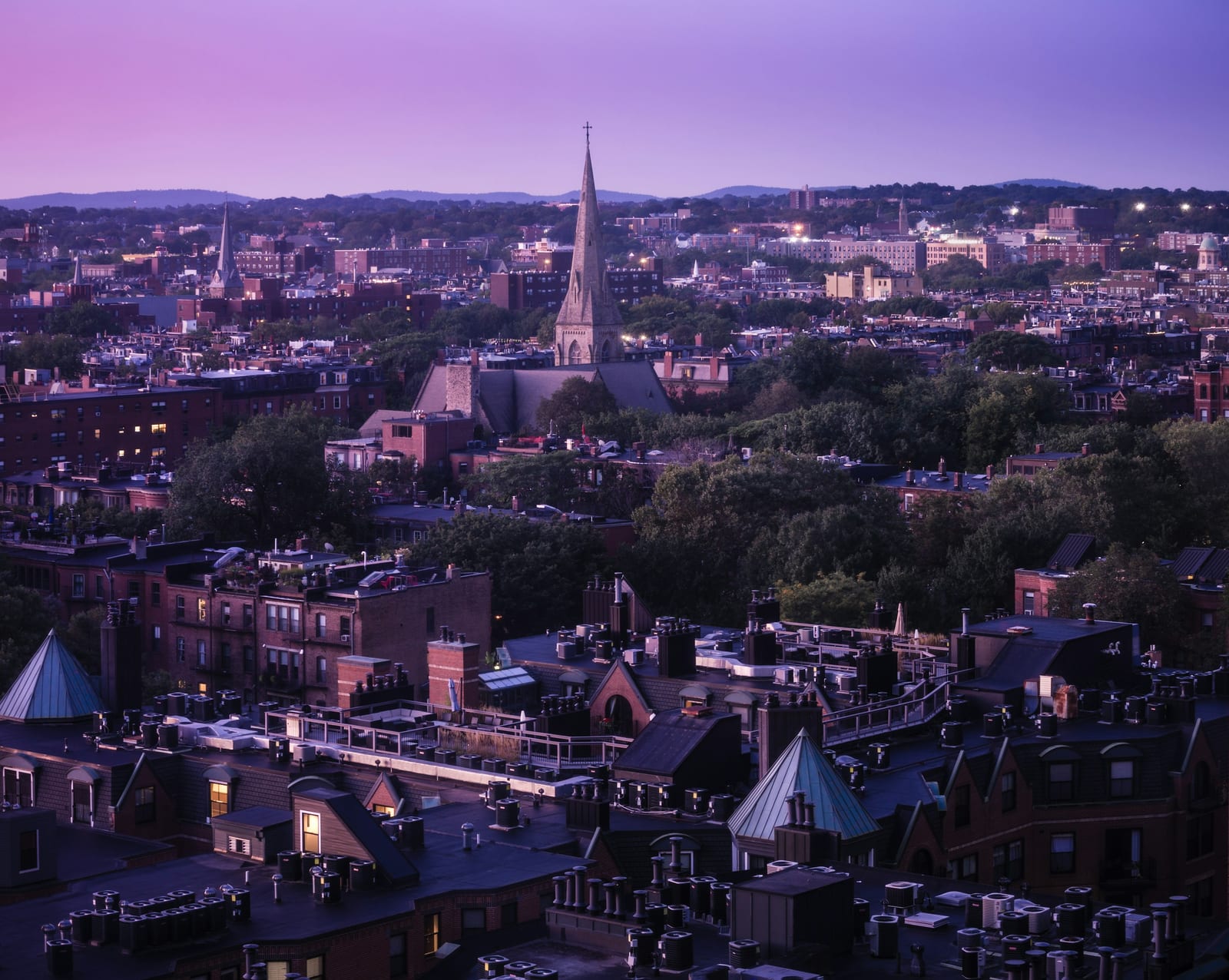 Golden-hour aerial view of Boston's South End, the Cathedral of the Holy Cross rising above Victorian rooftops