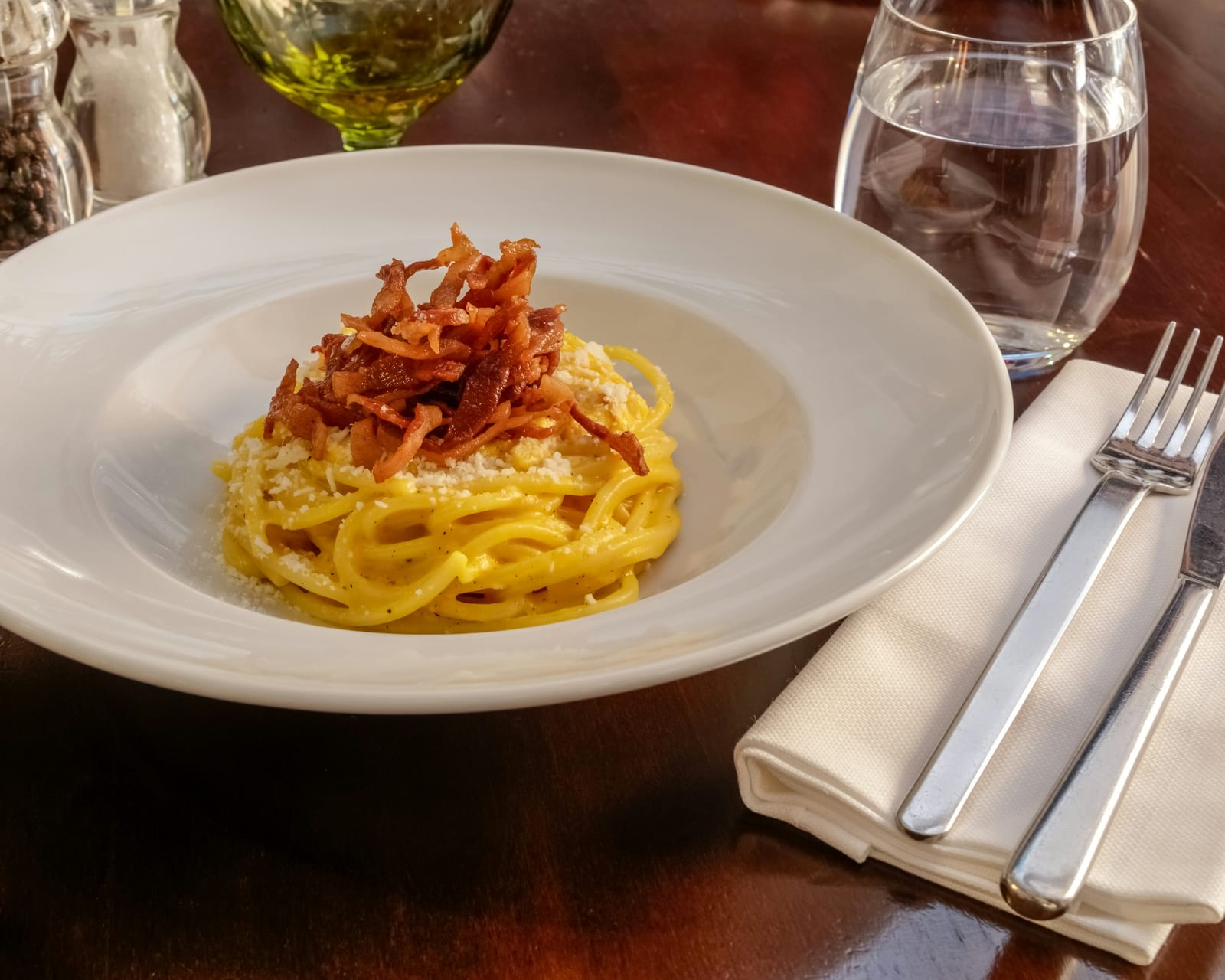 A plate of pasta alla gricia topped with crisp guanciale and pecorino, no tomato or egg.