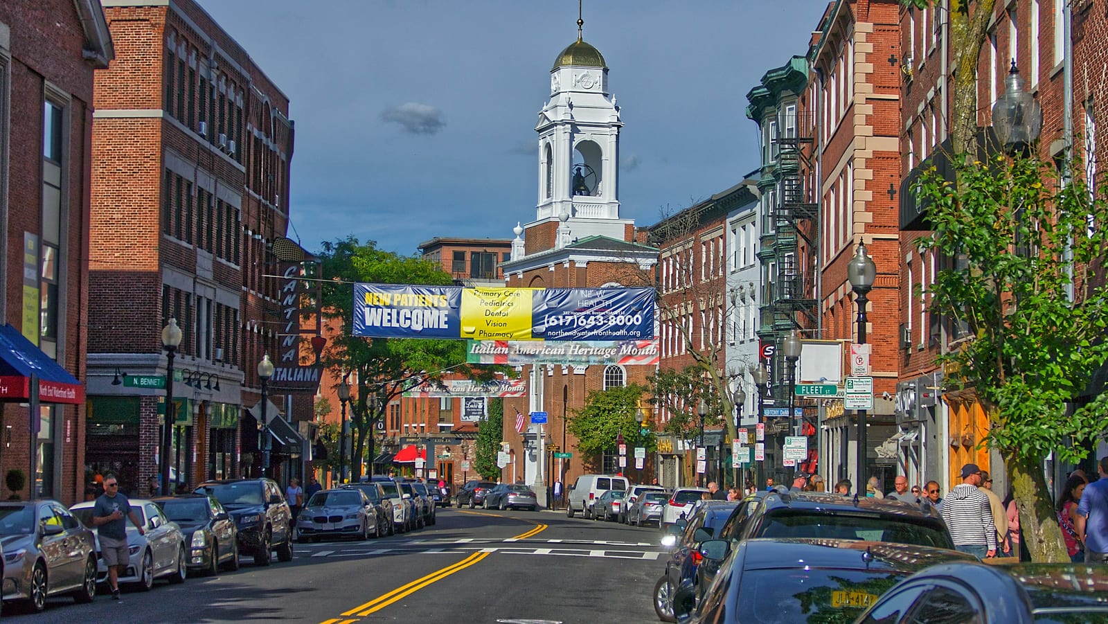 A historic brick-lined New England town square with colonial architecture.