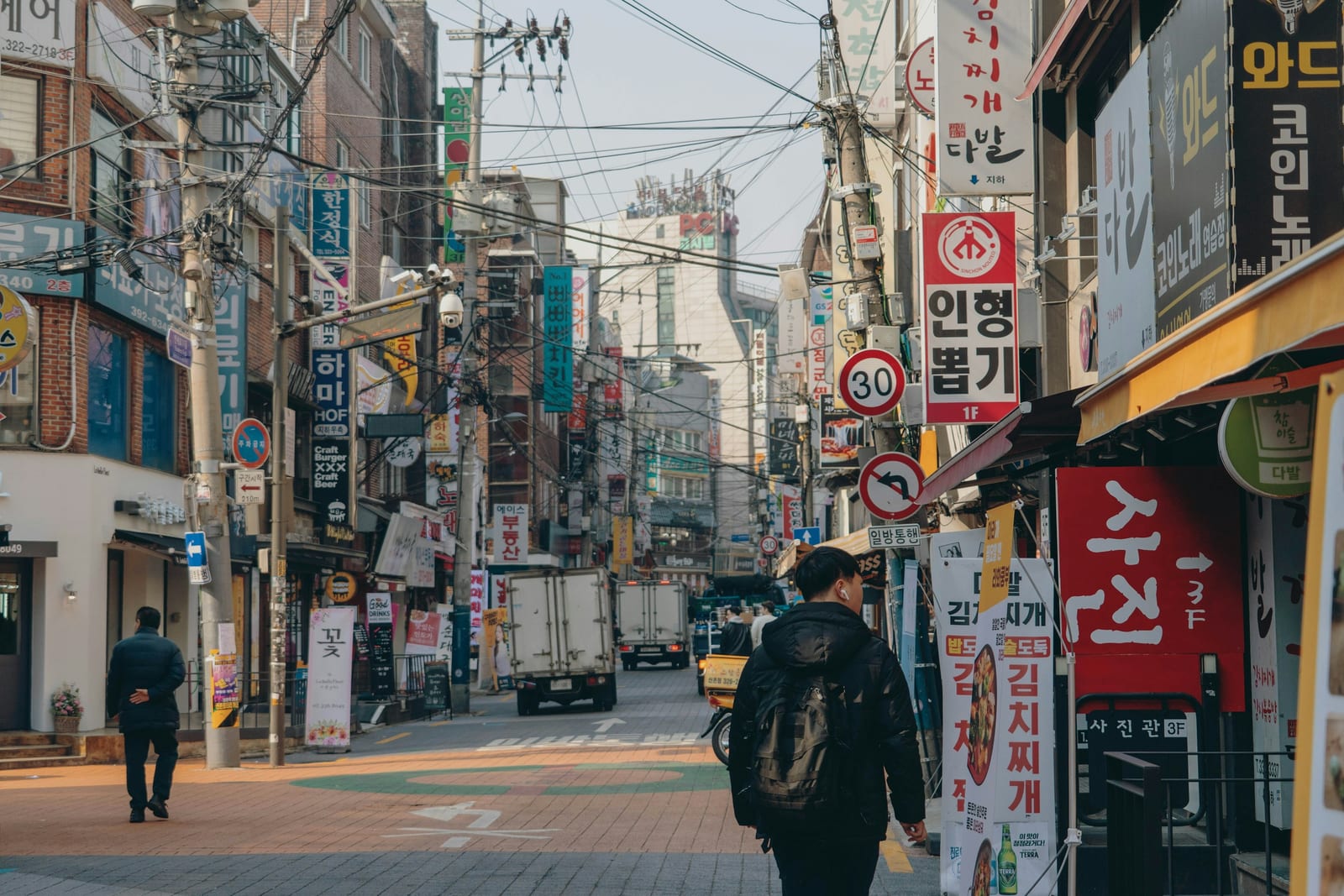 A commercial street in Hongdae lined with Korean signs, shops, utility wires, and pedestrians.