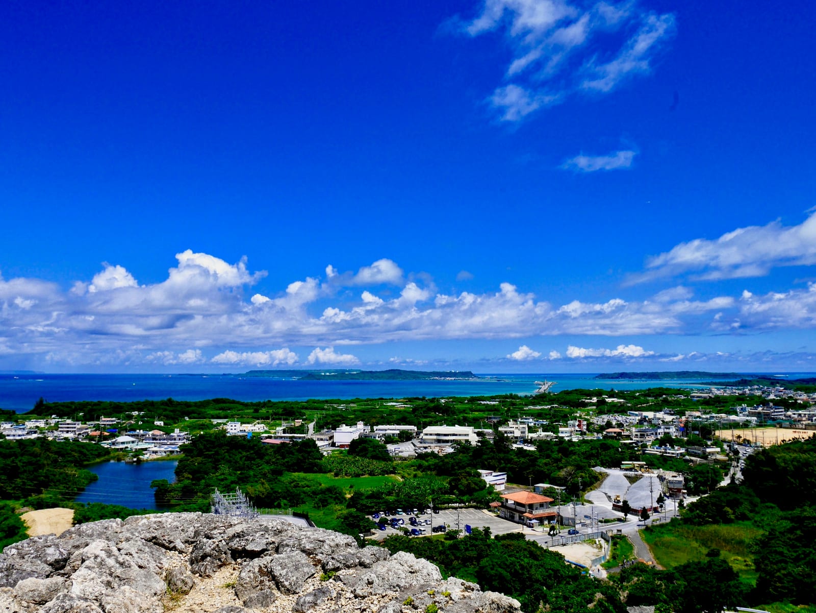 A coastal town and blue sea viewed from a rocky hillside beneath a bright blue sky.