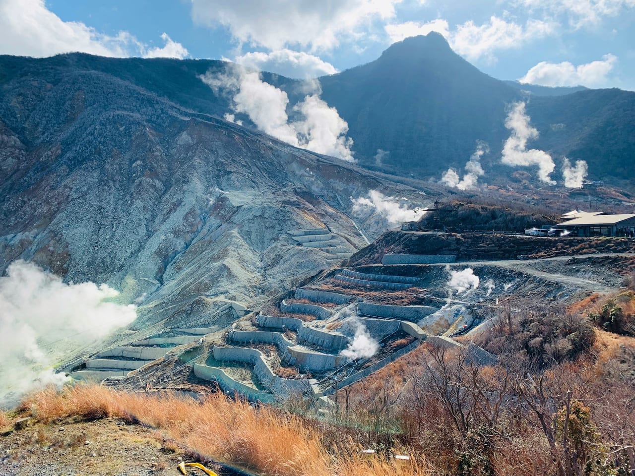 White sulphur steam rises from the barren slopes of the Owakudani volcanic valley under a blue sky.