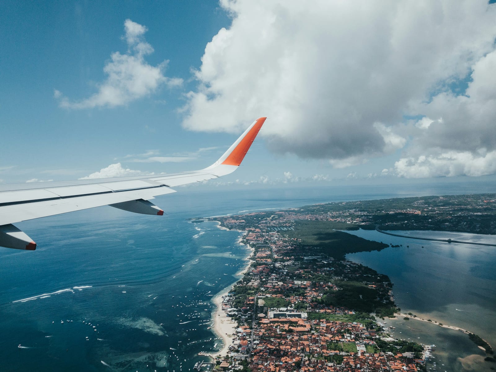 An airplane wing stretches over a tropical coastline, blue ocean, beaches, and densely settled islands.