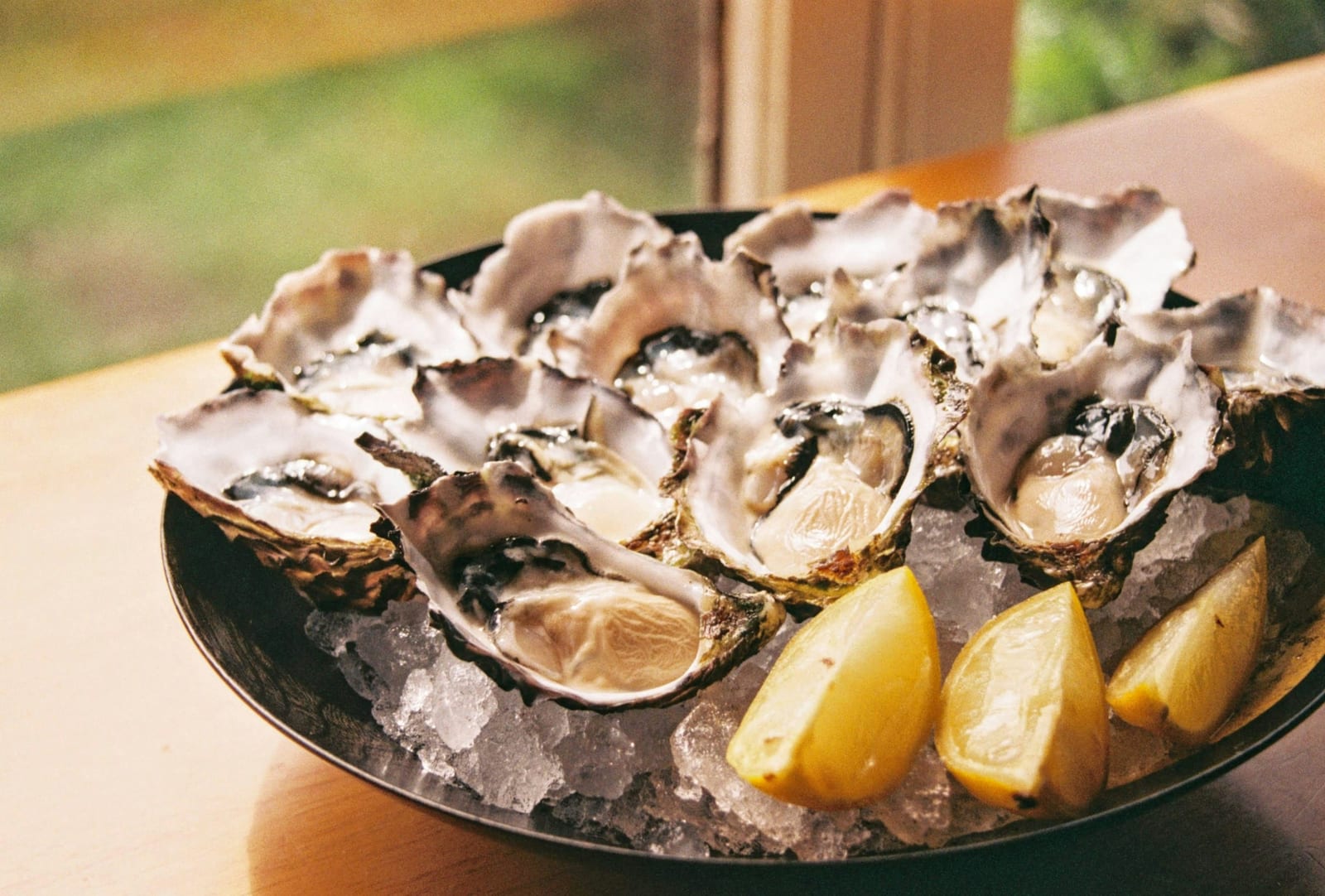 A platter of freshly shucked oysters on ice with lemon wedges.