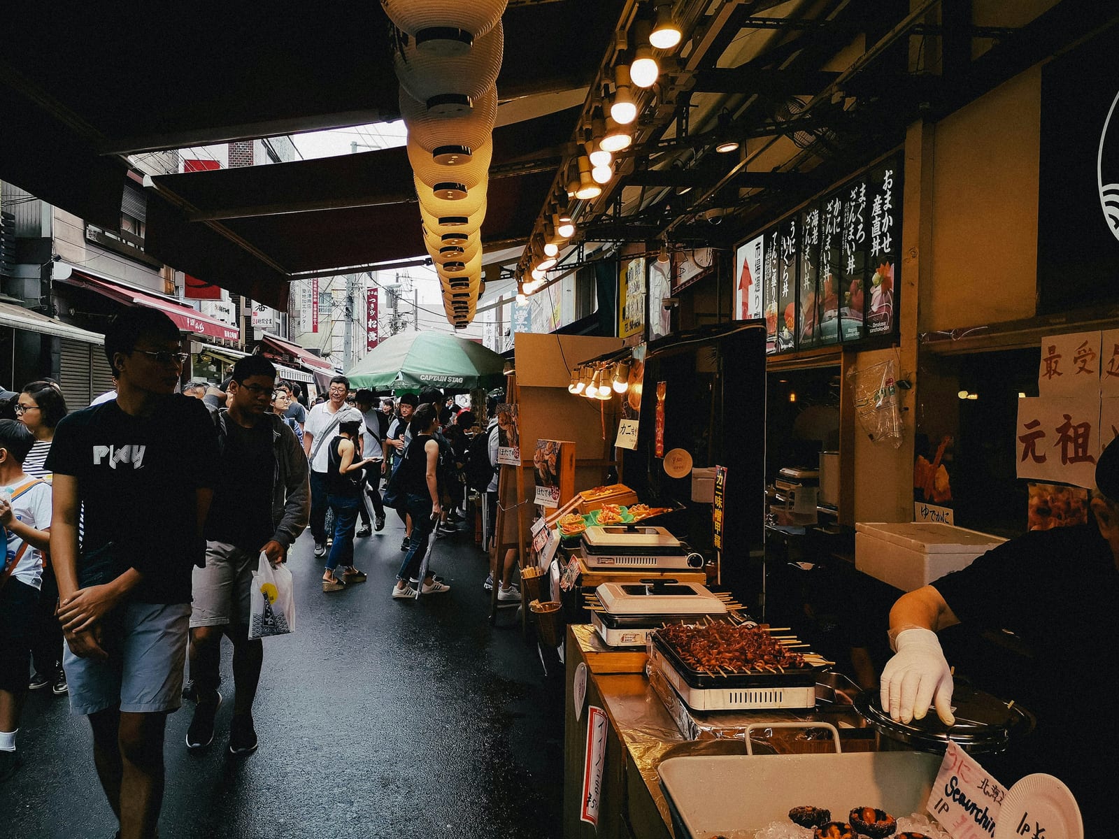 A covered market lane lined with food stalls selling grilled skewers as shoppers pass.