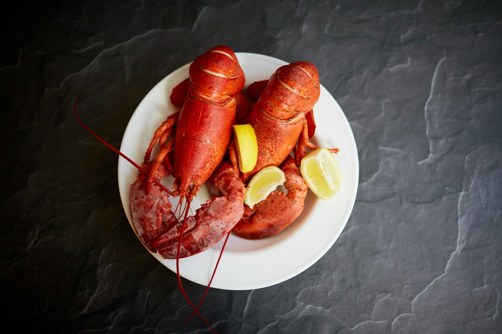 A whole lobster dinner with corn on the cob and drawn butter on a paper-covered table.