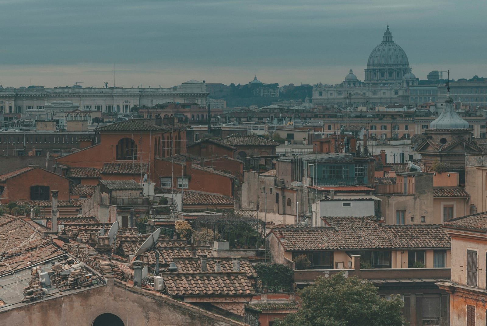 A panoramic view over Rome's rooftops to St Peter's dome, framed by trees turning autumn gold in Villa Borghese.