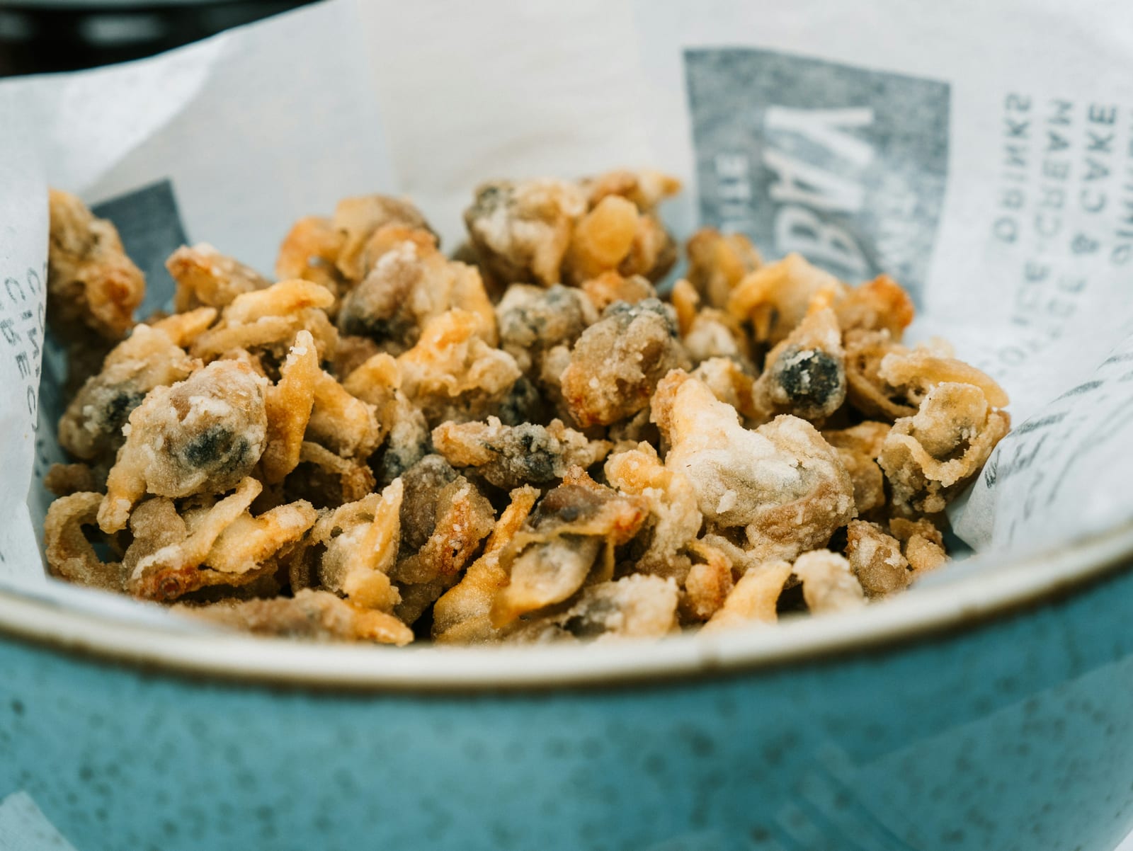 A paper-lined bowl holds a heap of golden whole-belly fried clams.
