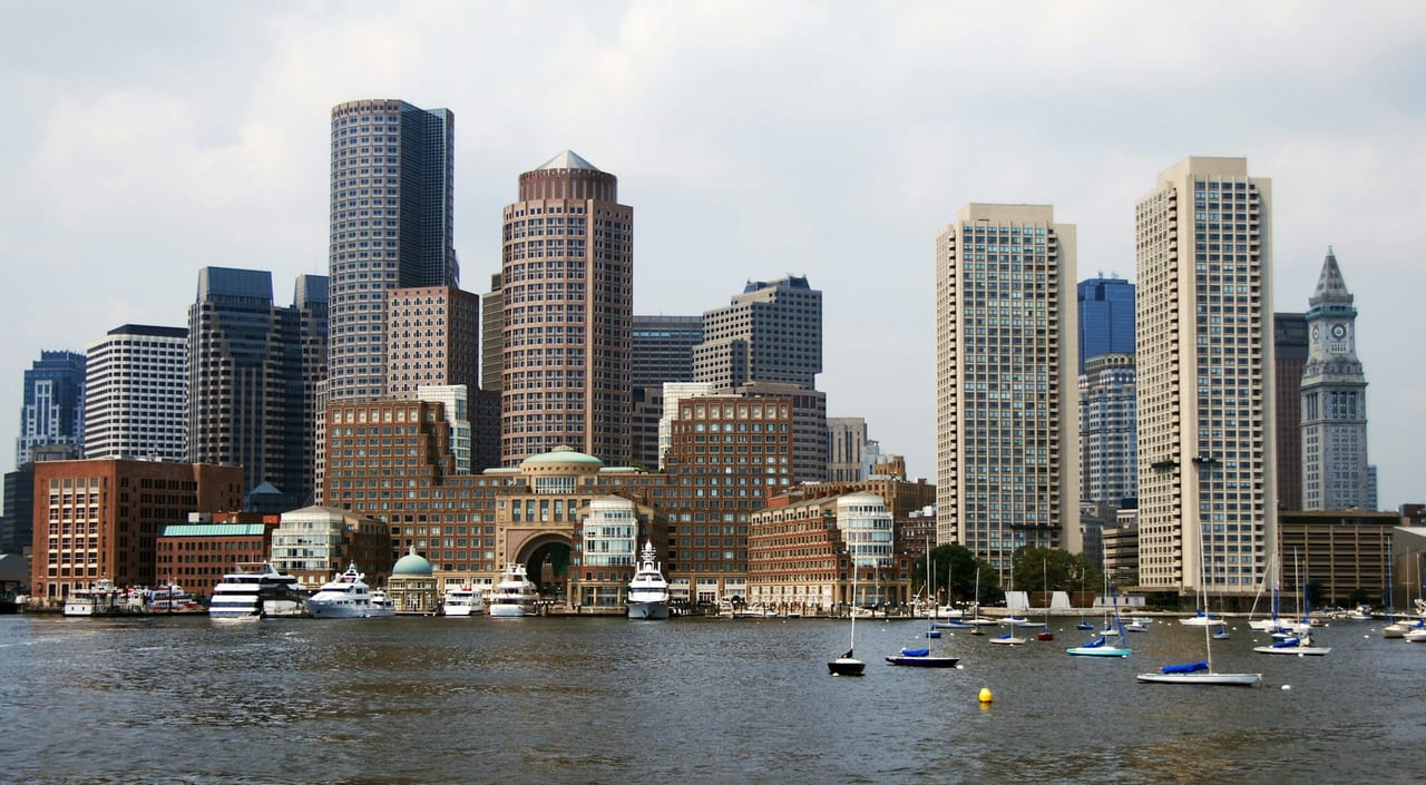 Boston's waterfront and harbor with sailboats and the city skyline in the background.