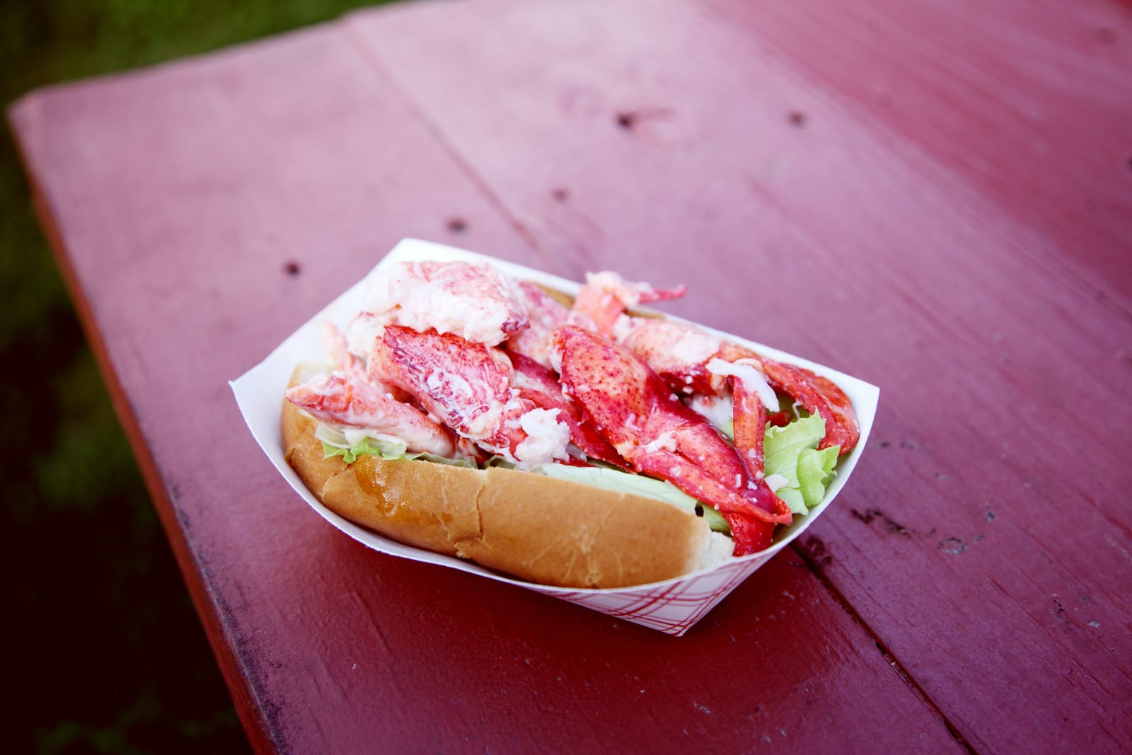A New England lobster roll with fries and a wedge of lemon on a paper-lined tray.