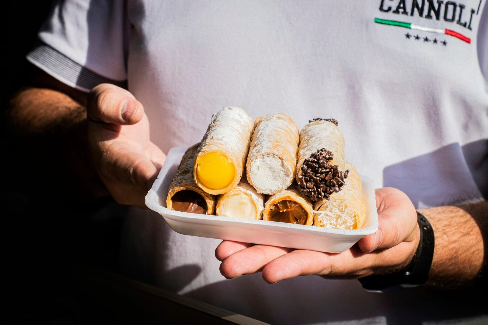 A tray of cannoli with ricotta filling, dusted with powdered sugar.
