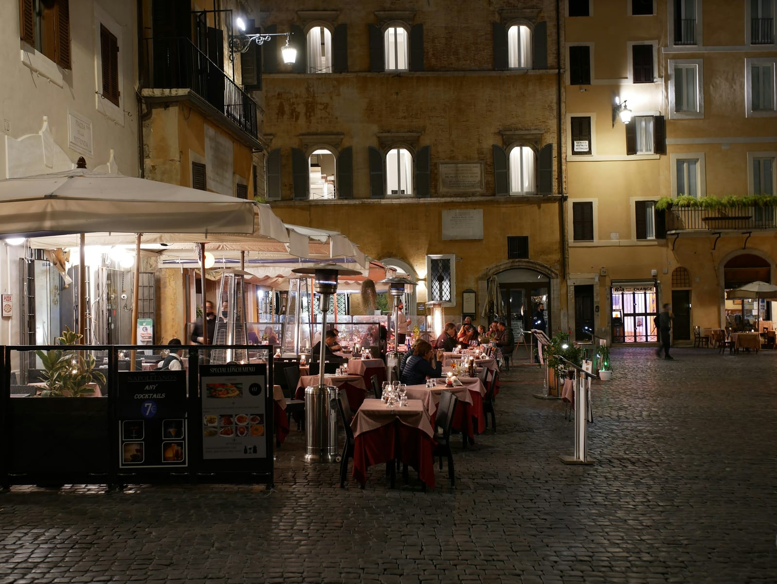 Diners at outdoor tables along a Trastevere lane in the evening.