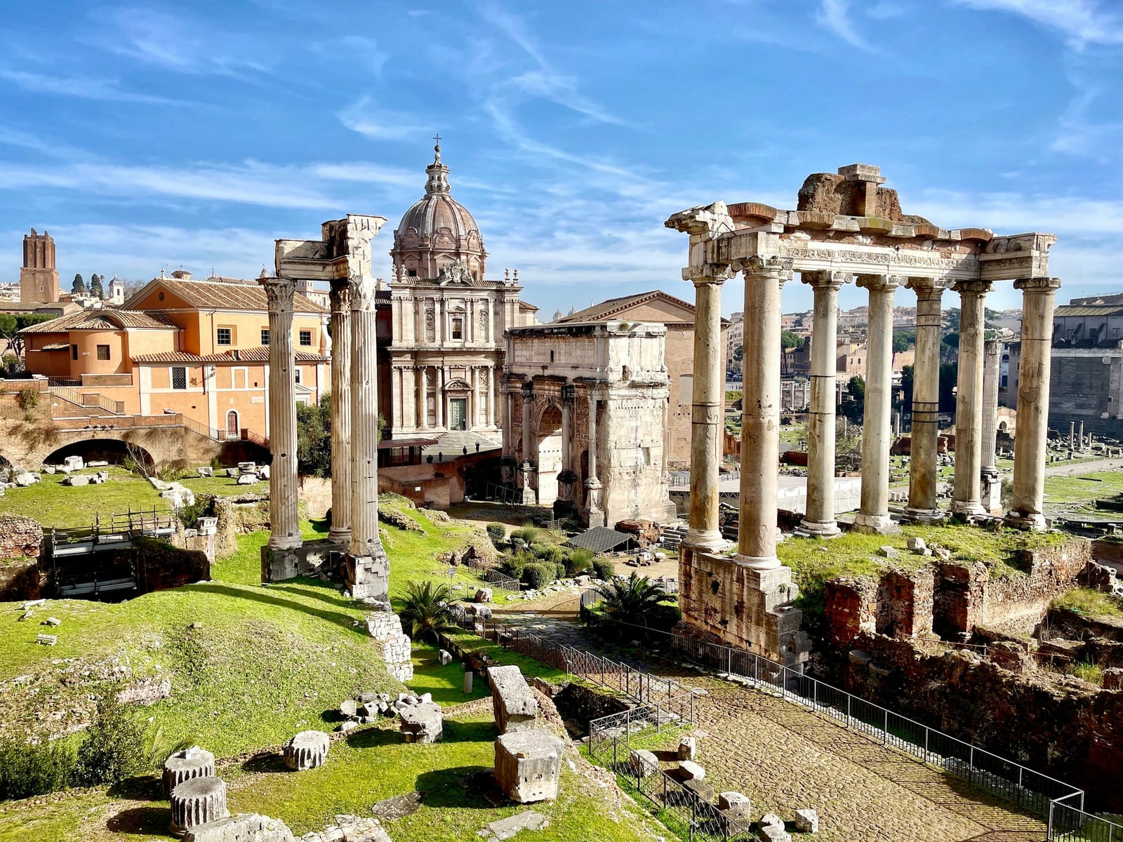 Standing columns and ruins of the Roman Forum under a blue sky.