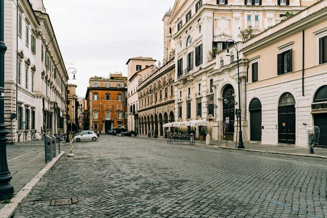 A cobblestone Monti lane with cafe stools set out along ochre buildings.
