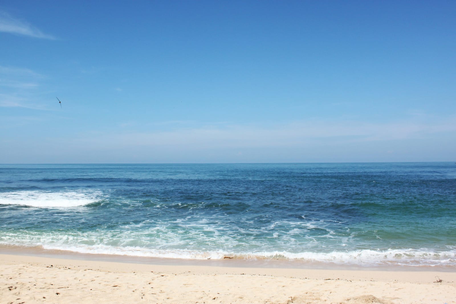 A sandy beach with waves breaking along the ocean shore under a clear blue sky.