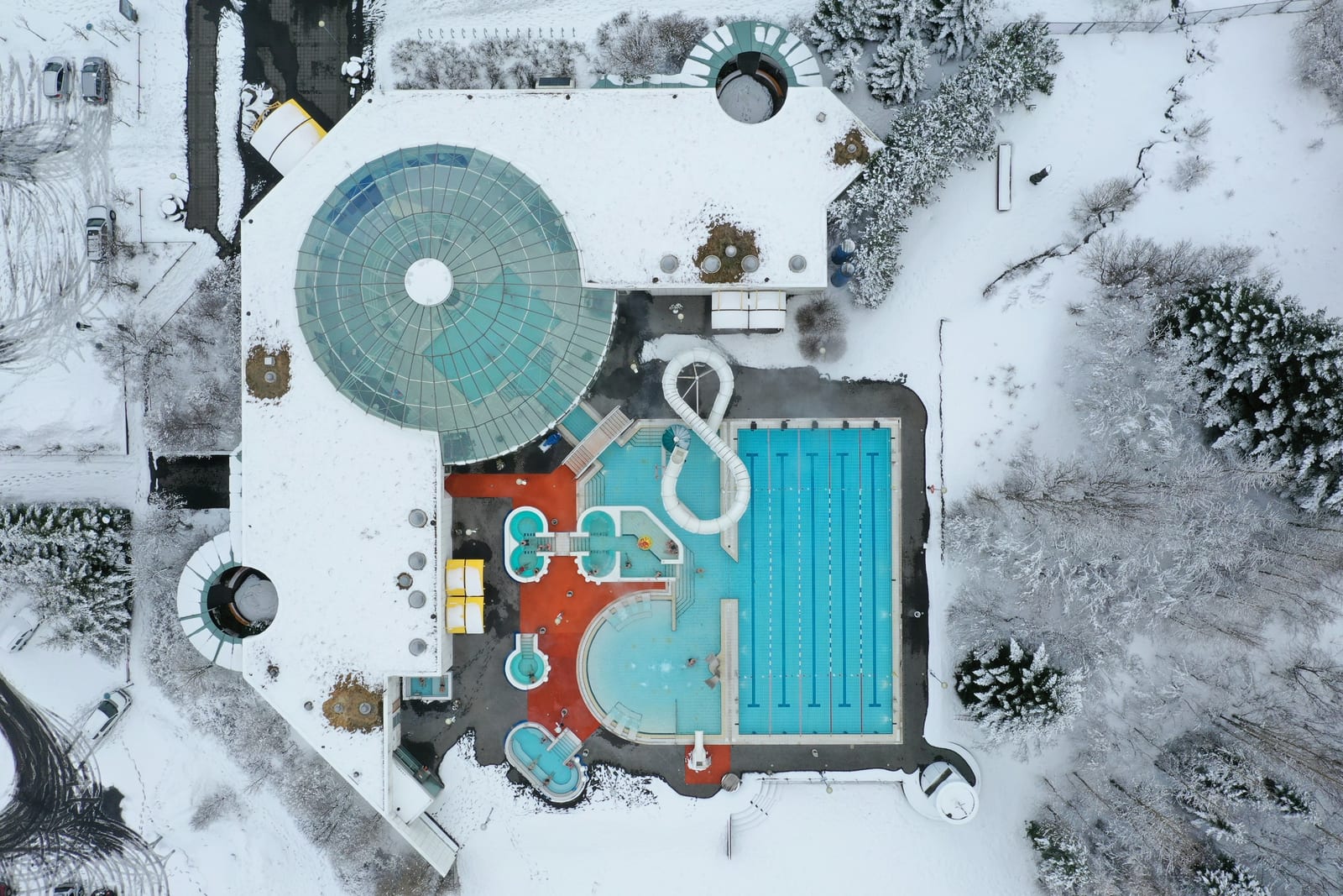 Aerial view of a turquoise geothermal swimming pool complex surrounded by snow.