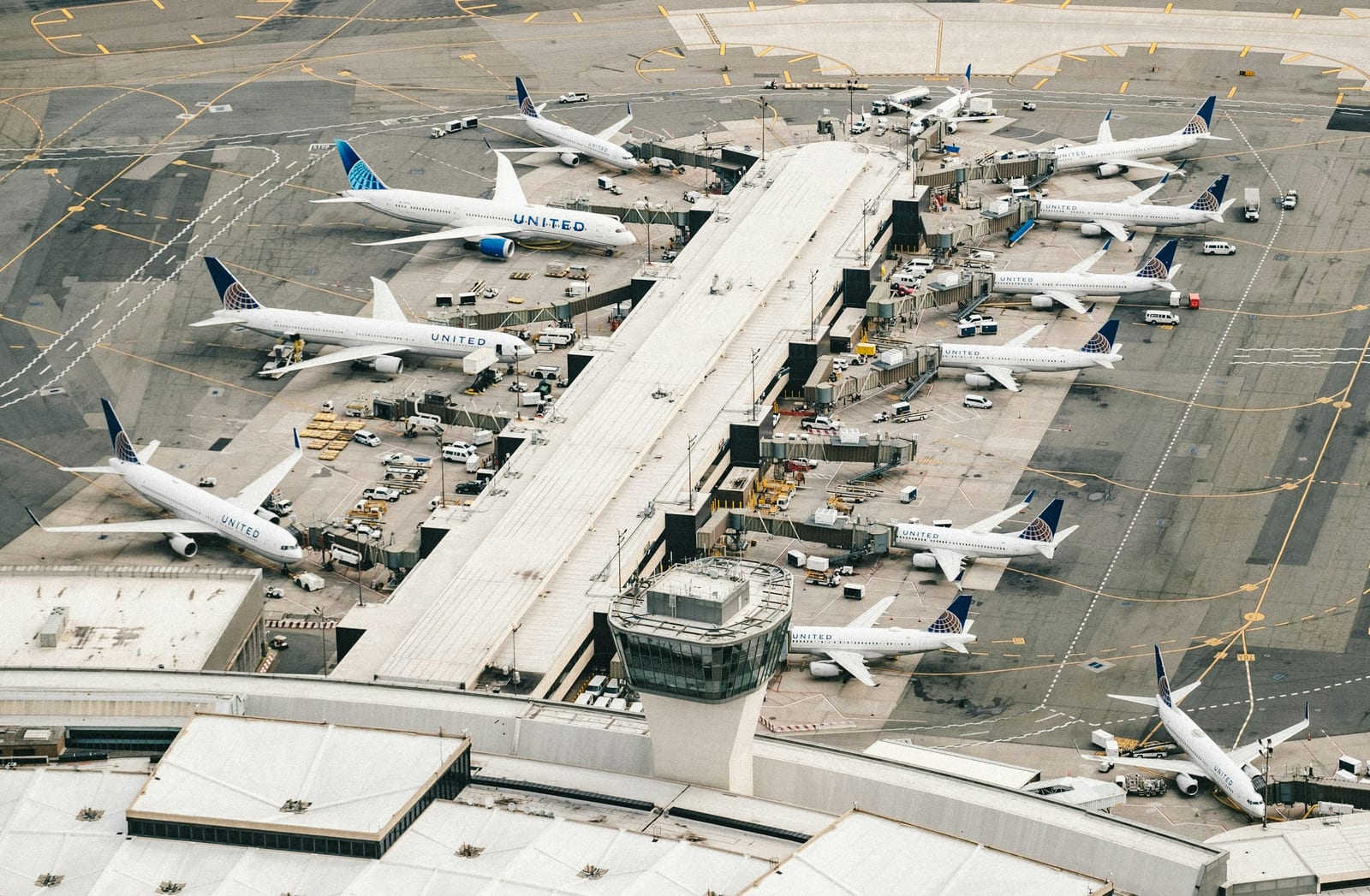 Aerial view of an airport terminal surrounded by parked passenger aircraft and service vehicles.