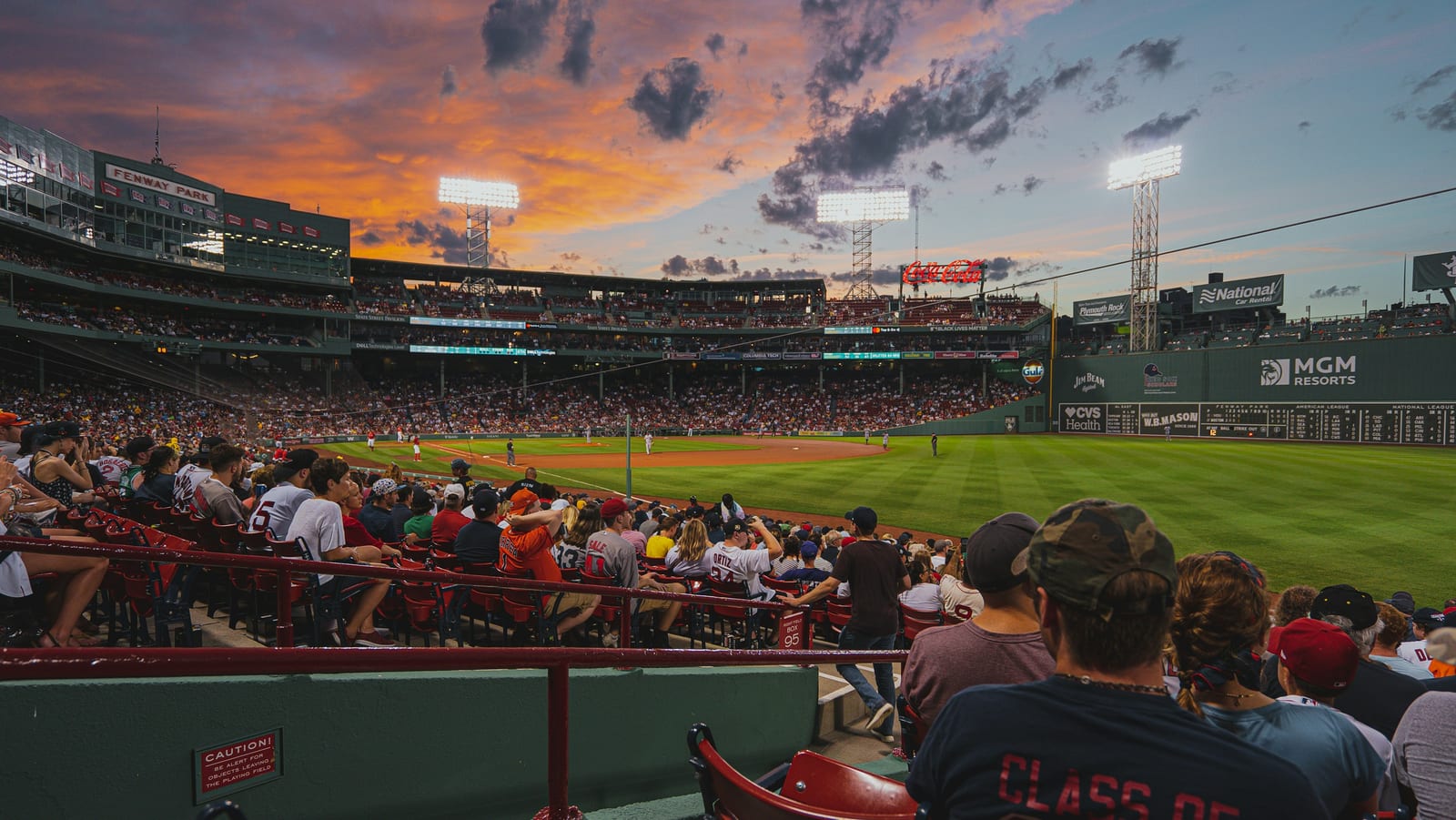Fenway Park packed with fans on a summer evening, the Green Monster in full view.