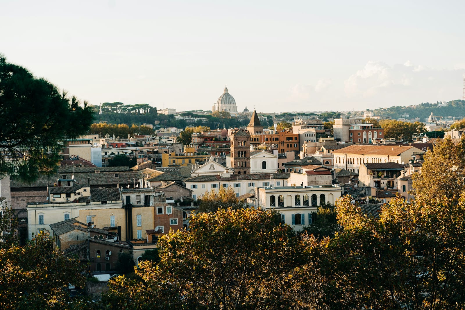 Autumn-gold trees framing a rooftop view across Rome to St Peter's dome from the Pincio.