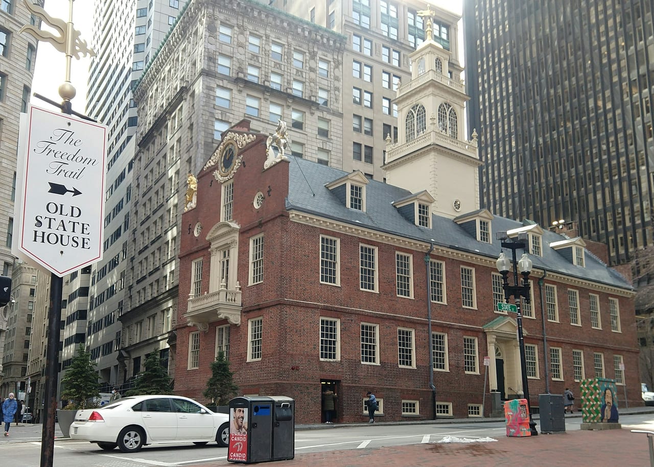 The Freedom Trail's red-brick line winds past the Old State House in downtown Boston under a bright sky.