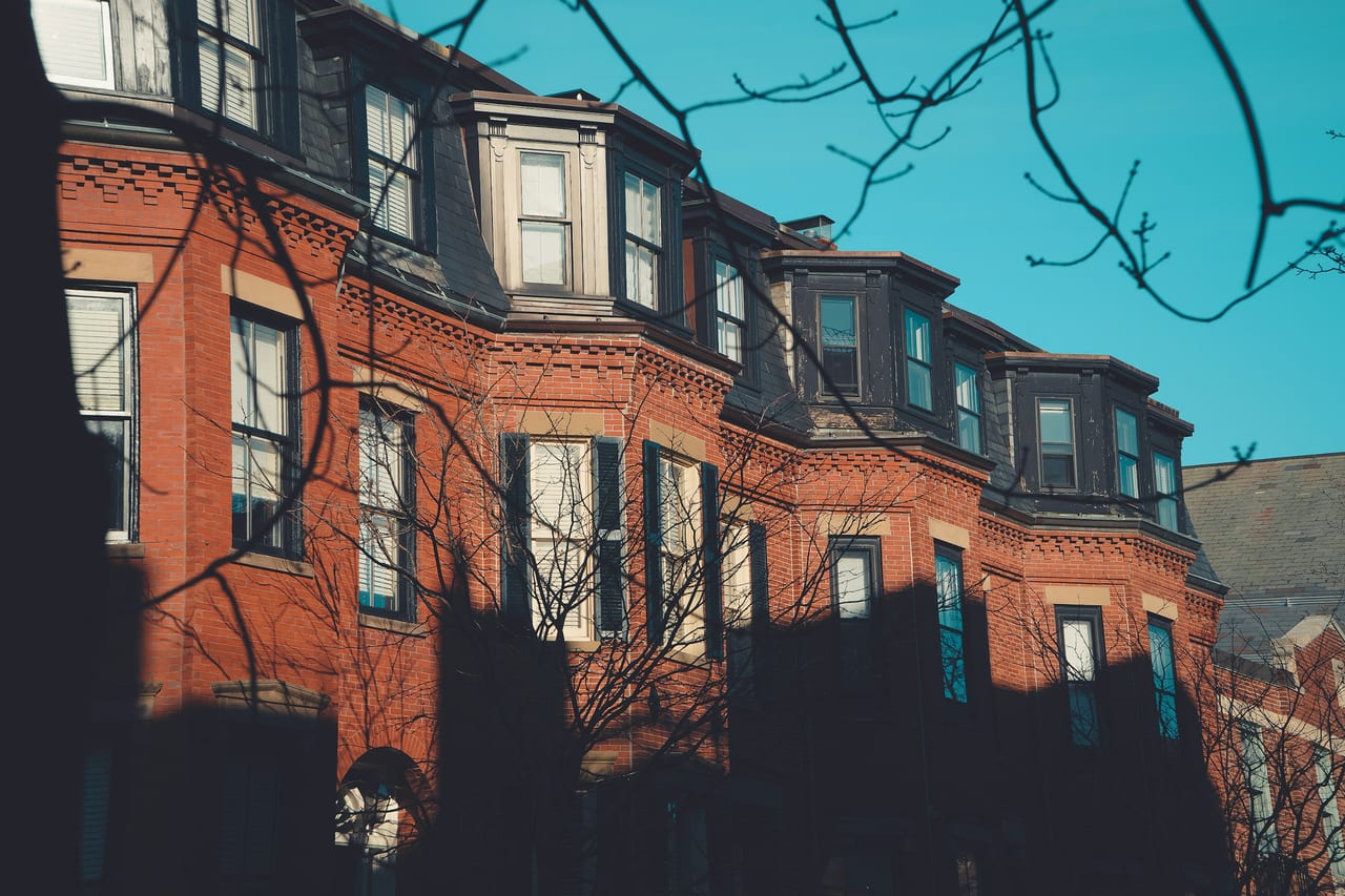 Brick rowhouses line a tree-shaded street in Boston's Back Bay neighborhood on a clear autumn day.