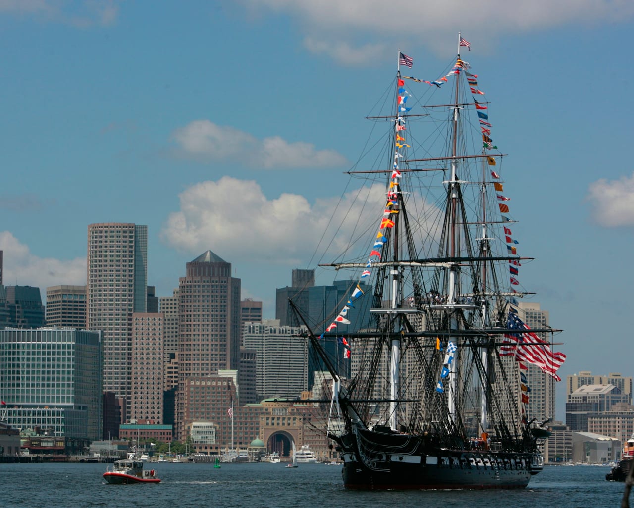 The USS Constitution's dark hull and tall masts rise above the dock at the Charlestown Navy Yard.