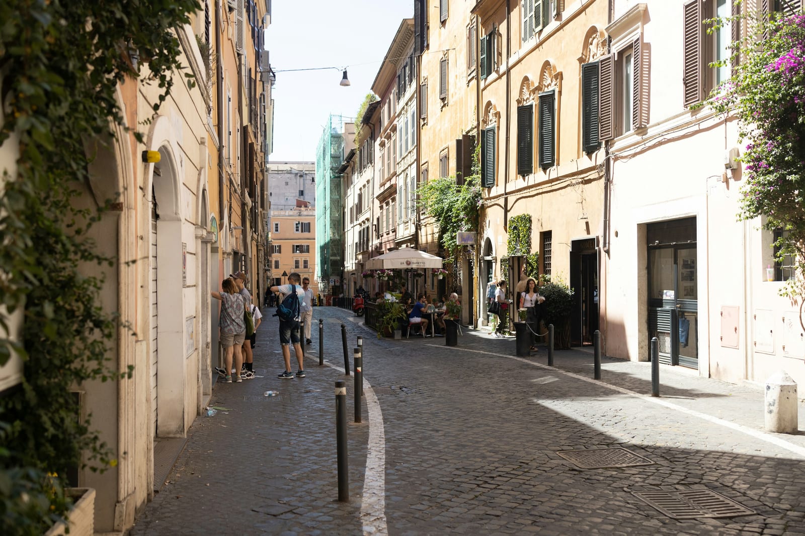A cobblestone Monti lane with cafe stools set out along ochre buildings.