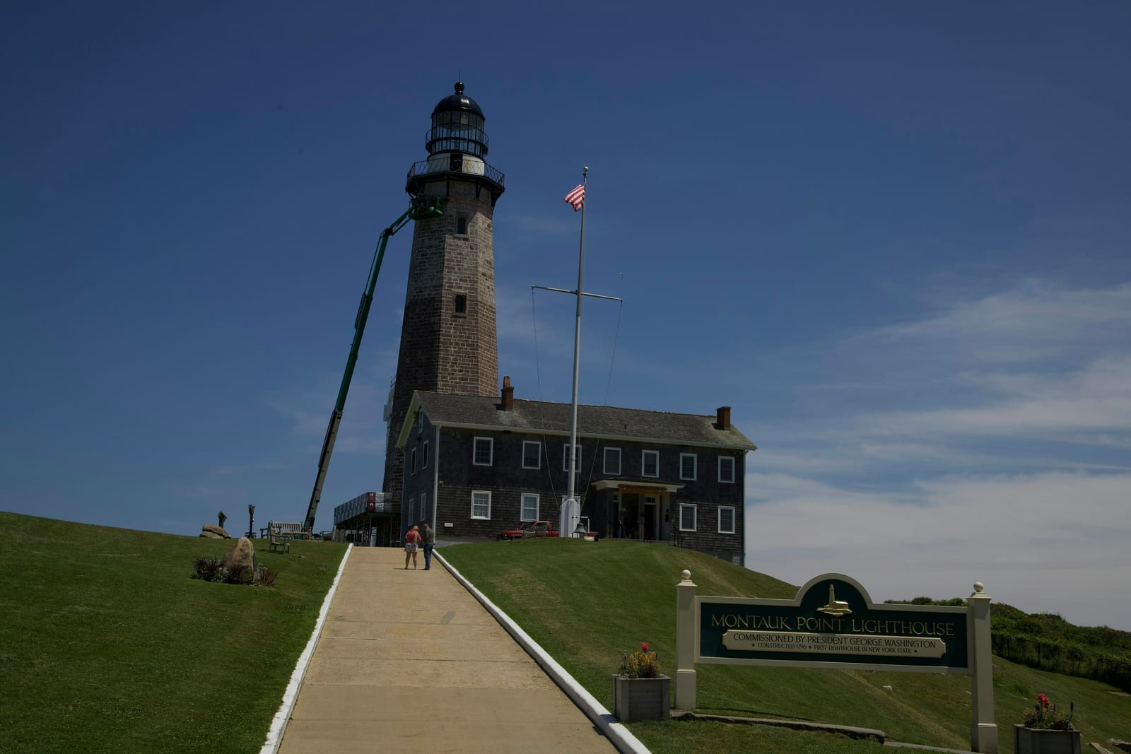 Montauk Lighthouse stands on a grassy rise beside its keeper's house under a blue sky.