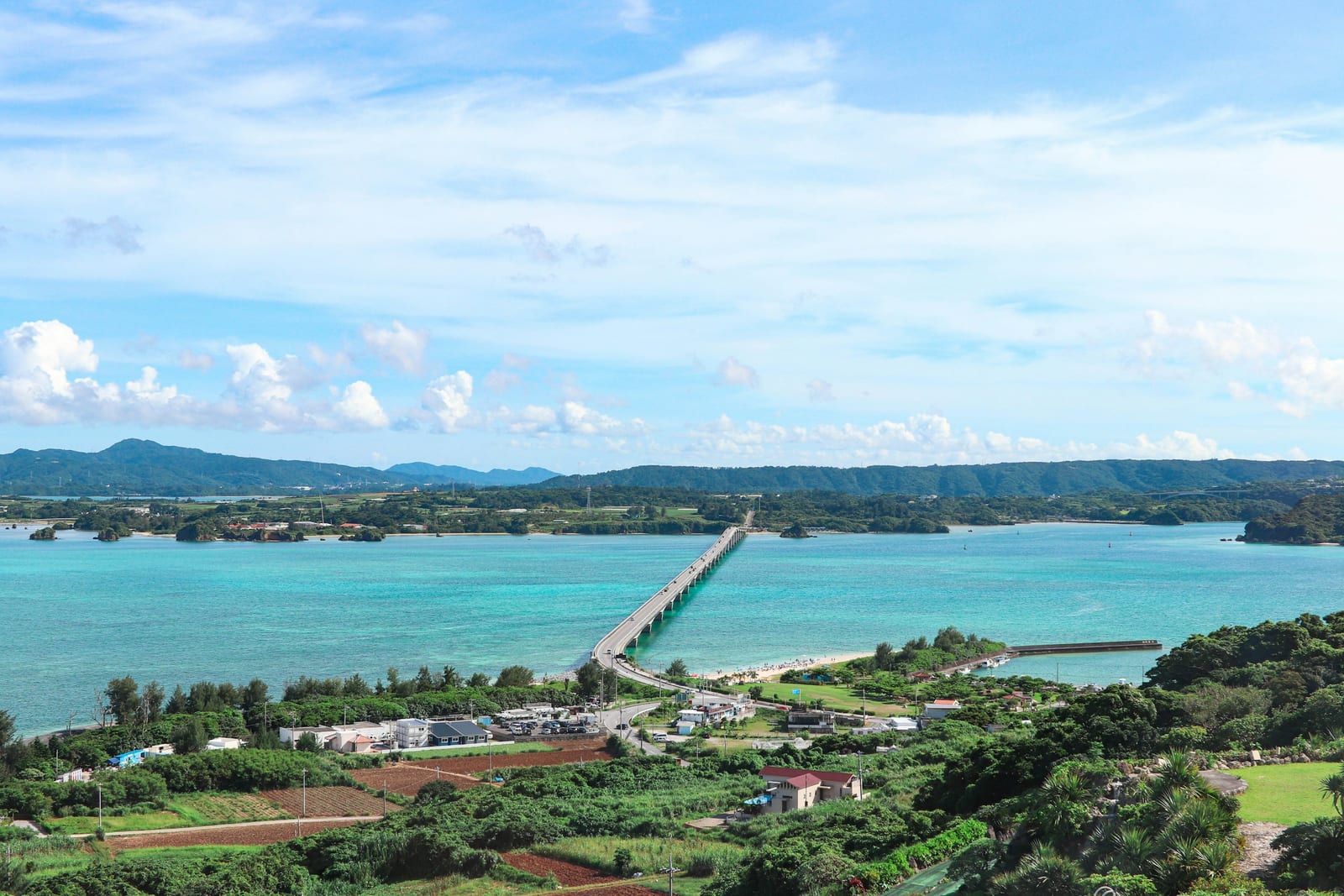 A long bridge crosses turquoise water between green Okinawan islands.