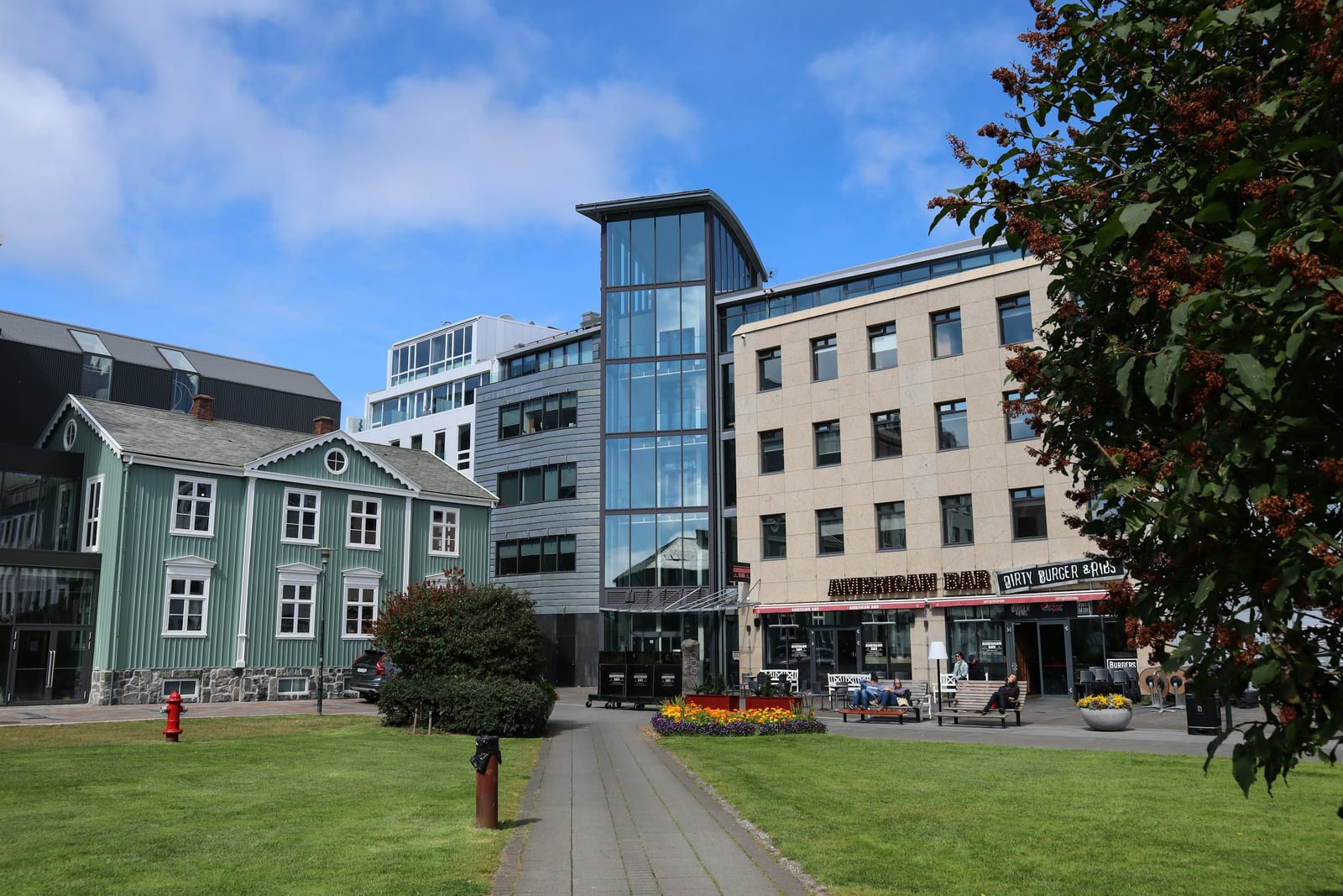A green park lawn and walkway framed by autumn foliage and Reykjavik buildings under a bright blue sky.