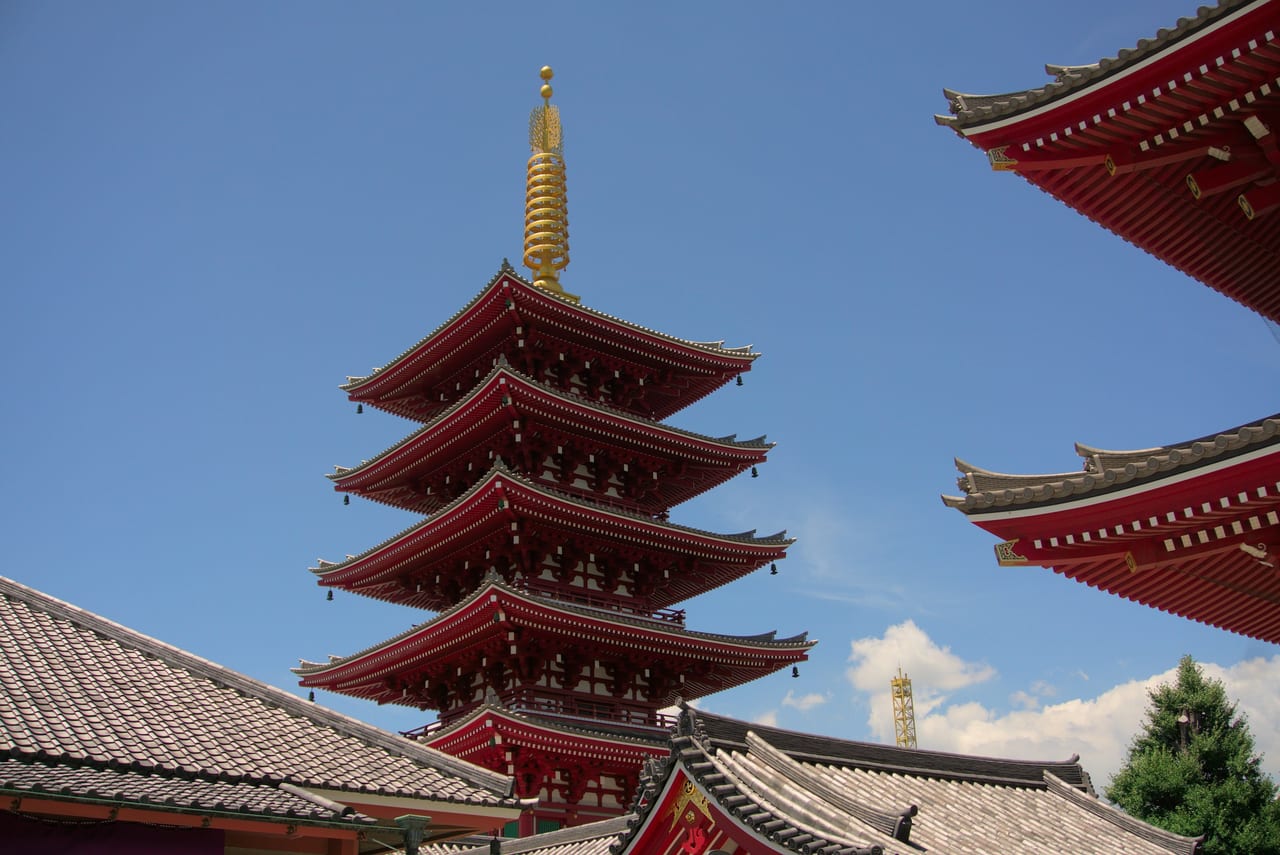 Senso-ji's vermilion five-story pagoda rises against a clear blue sky beside the temple's ornate eaves.