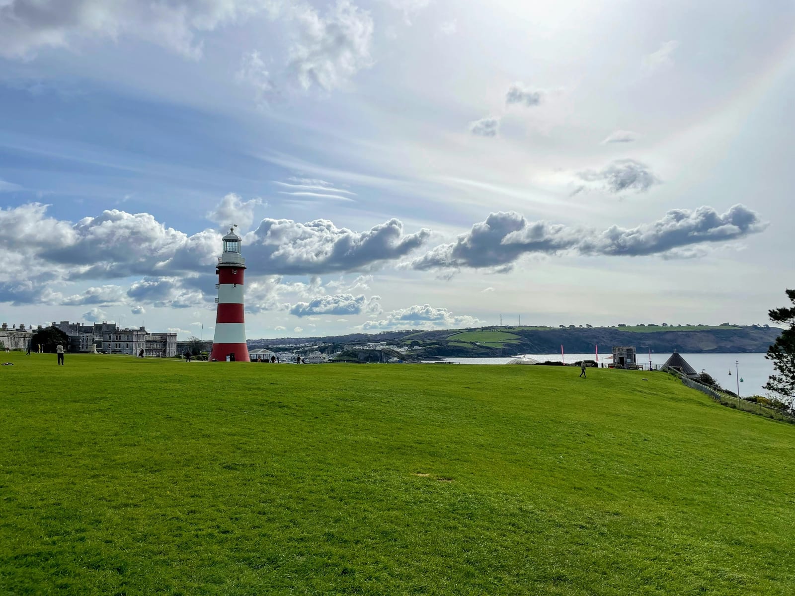A red-and-white striped lighthouse stands on a green lawn overlooking the water in Plymouth.