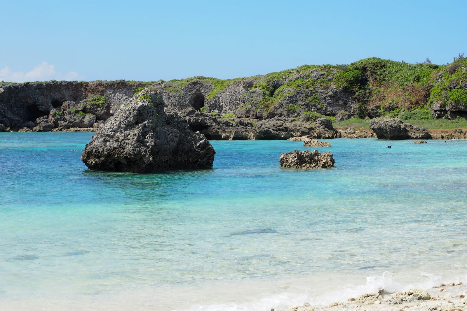 A bright sandy beach borders clear turquoise water and rocky coastal outcrops.