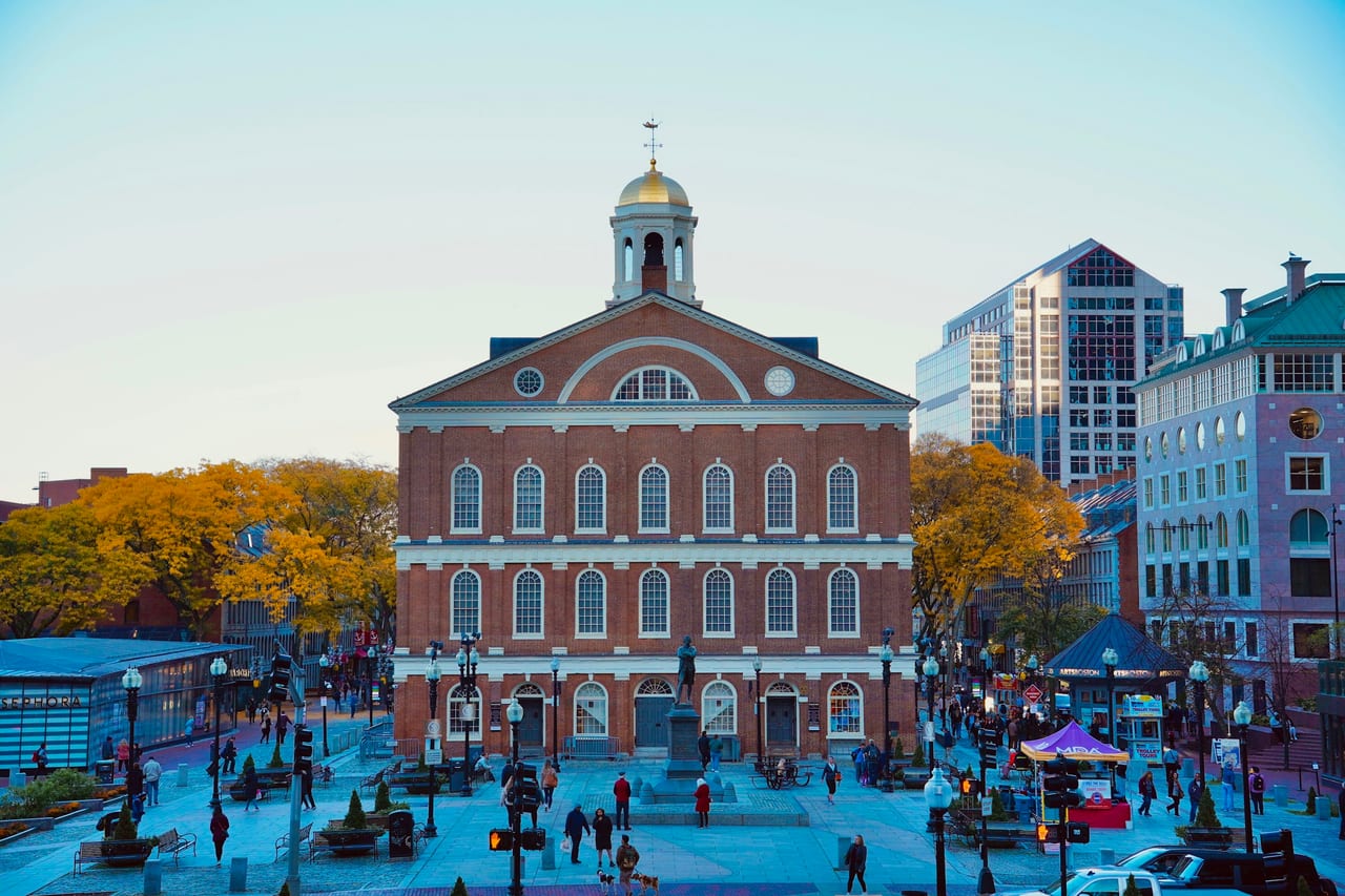 Faneuil Hall's brick facade and golden grasshopper weathervane stand against a blue sky in downtown Boston.
