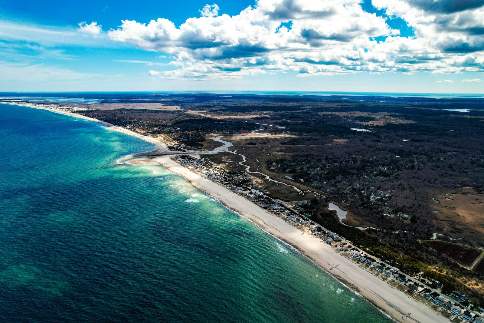 Aerial view of a long sandy shoreline meeting deep blue ocean under a partly cloudy sky.