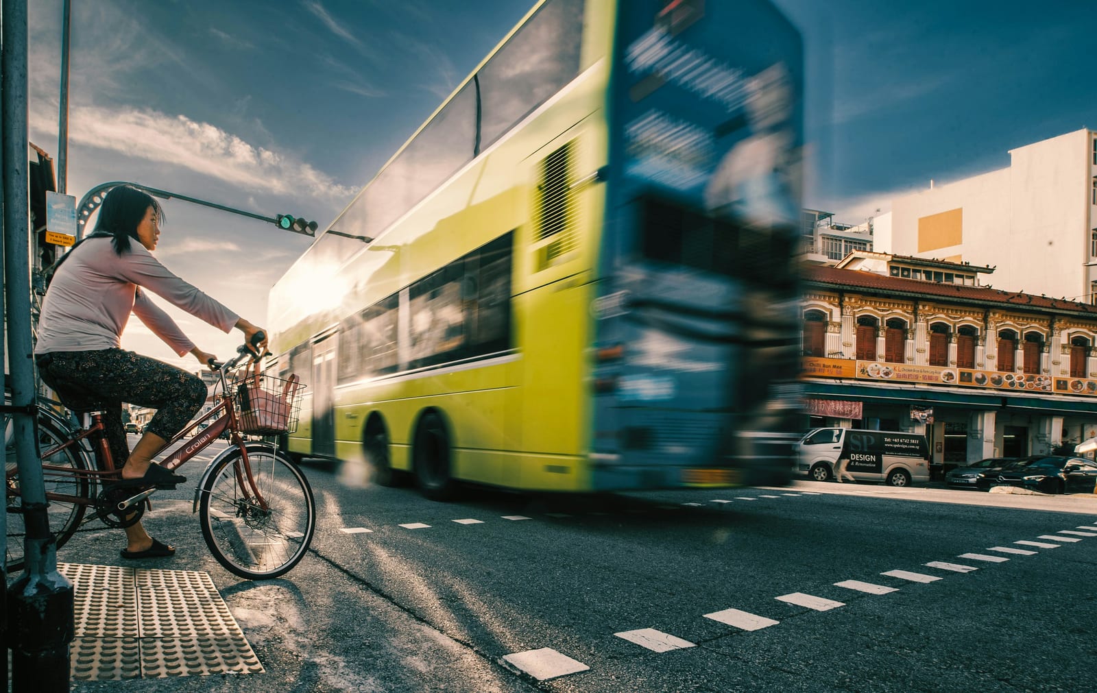 A cyclist rides beside a bright lime-green city bus at a marked urban intersection.