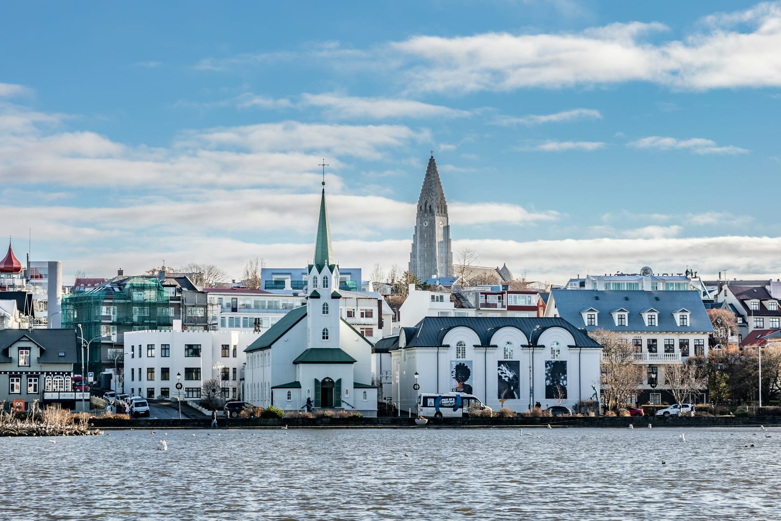 Reykjavik's waterfront buildings and Hallgrímskirkja stand beside the water under a blue sky.