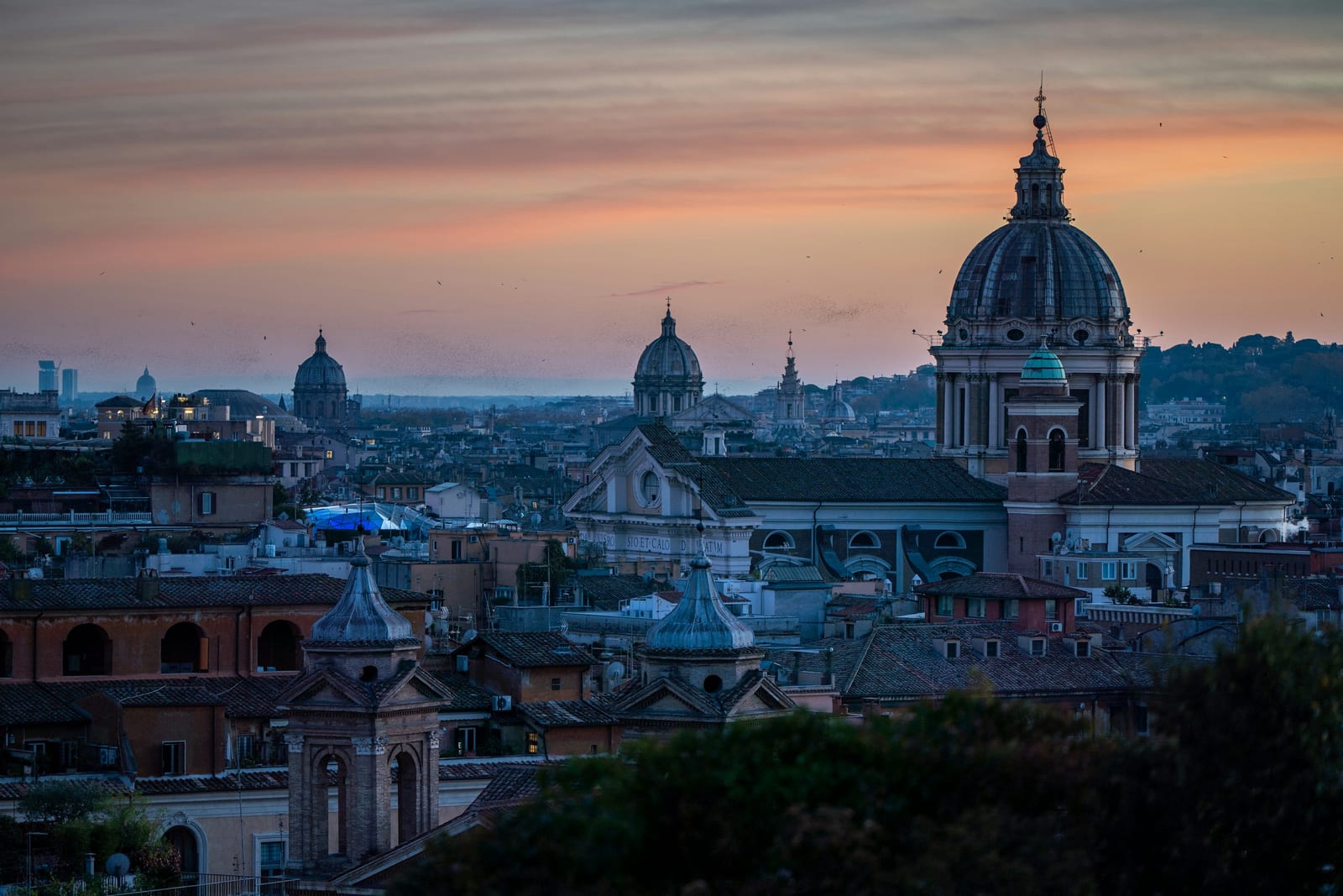 Rome's rooftops and church domes glowing under a golden sunset sky.