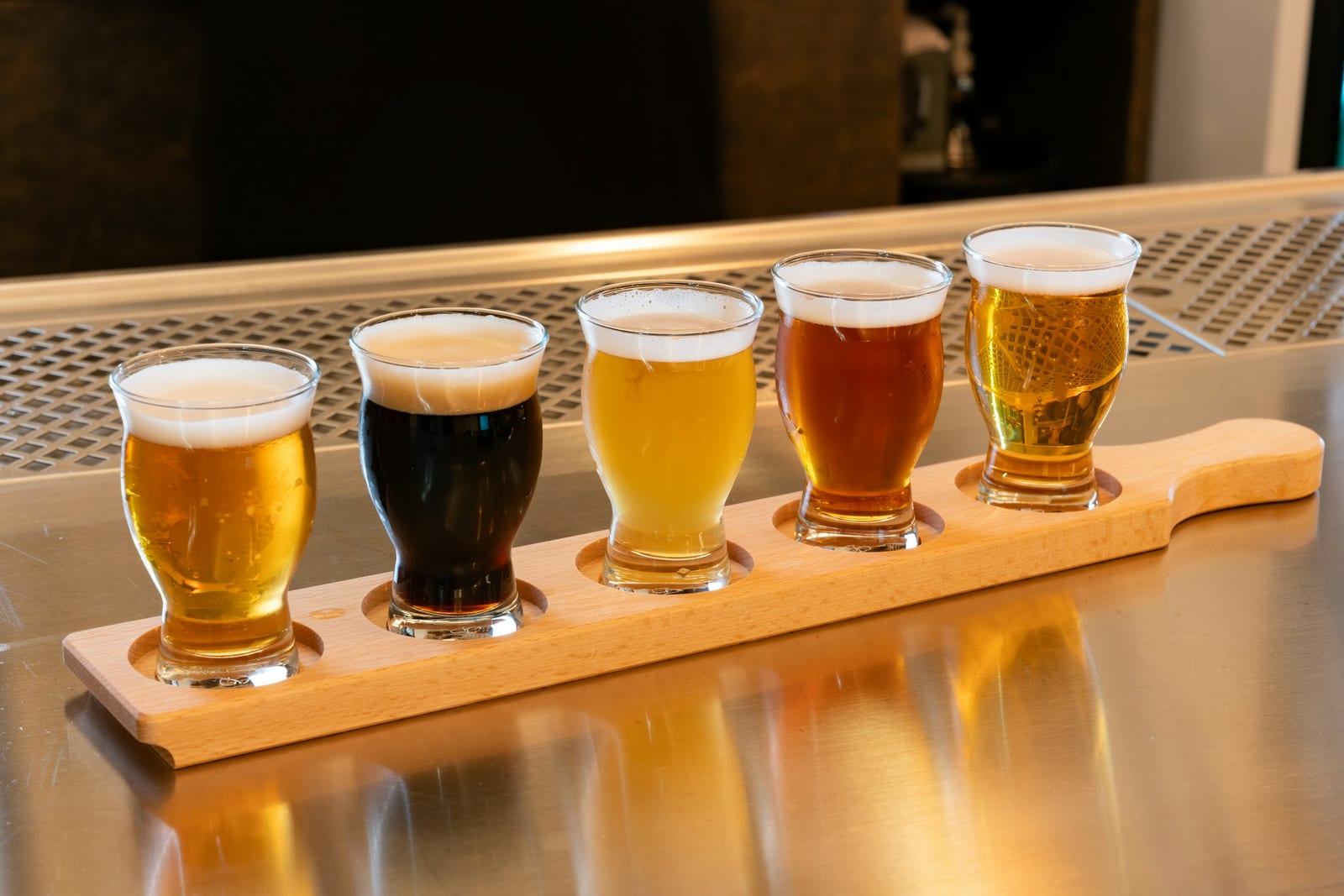 A flight of craft beer in small glasses on a wooden paddle at a taproom.