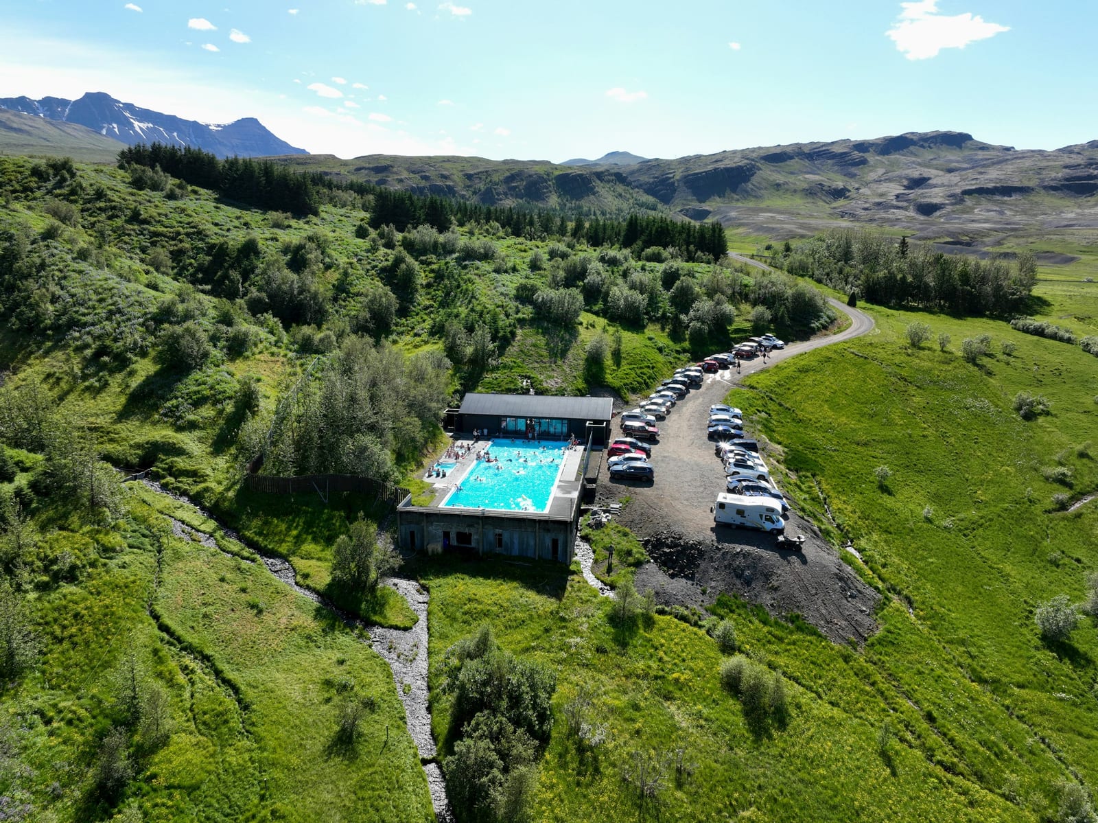 Aerial view of a bright turquoise outdoor pool beside a rural road in Iceland’s green countryside.