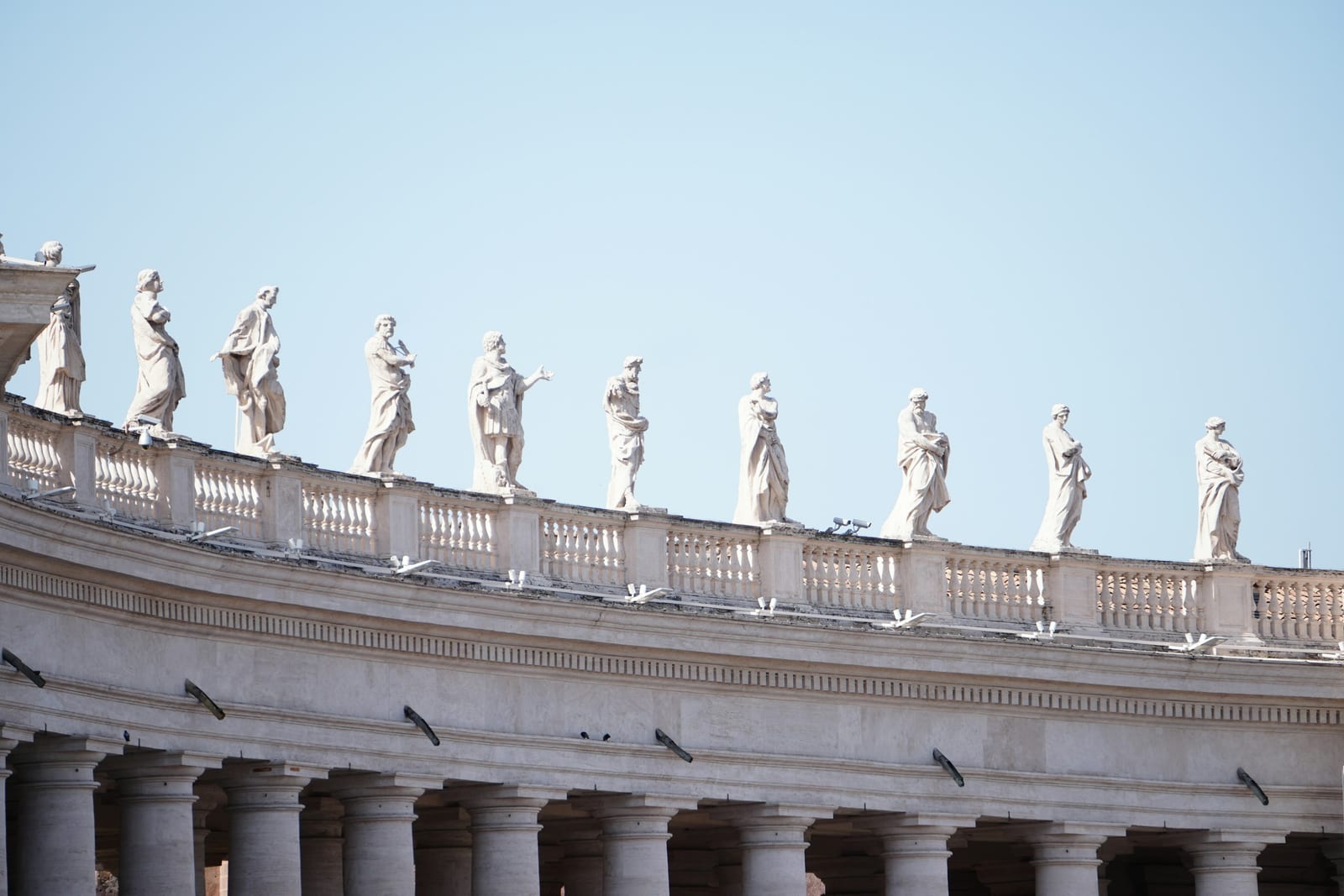 The statues along St Peter's colonnade against a clear blue sky.