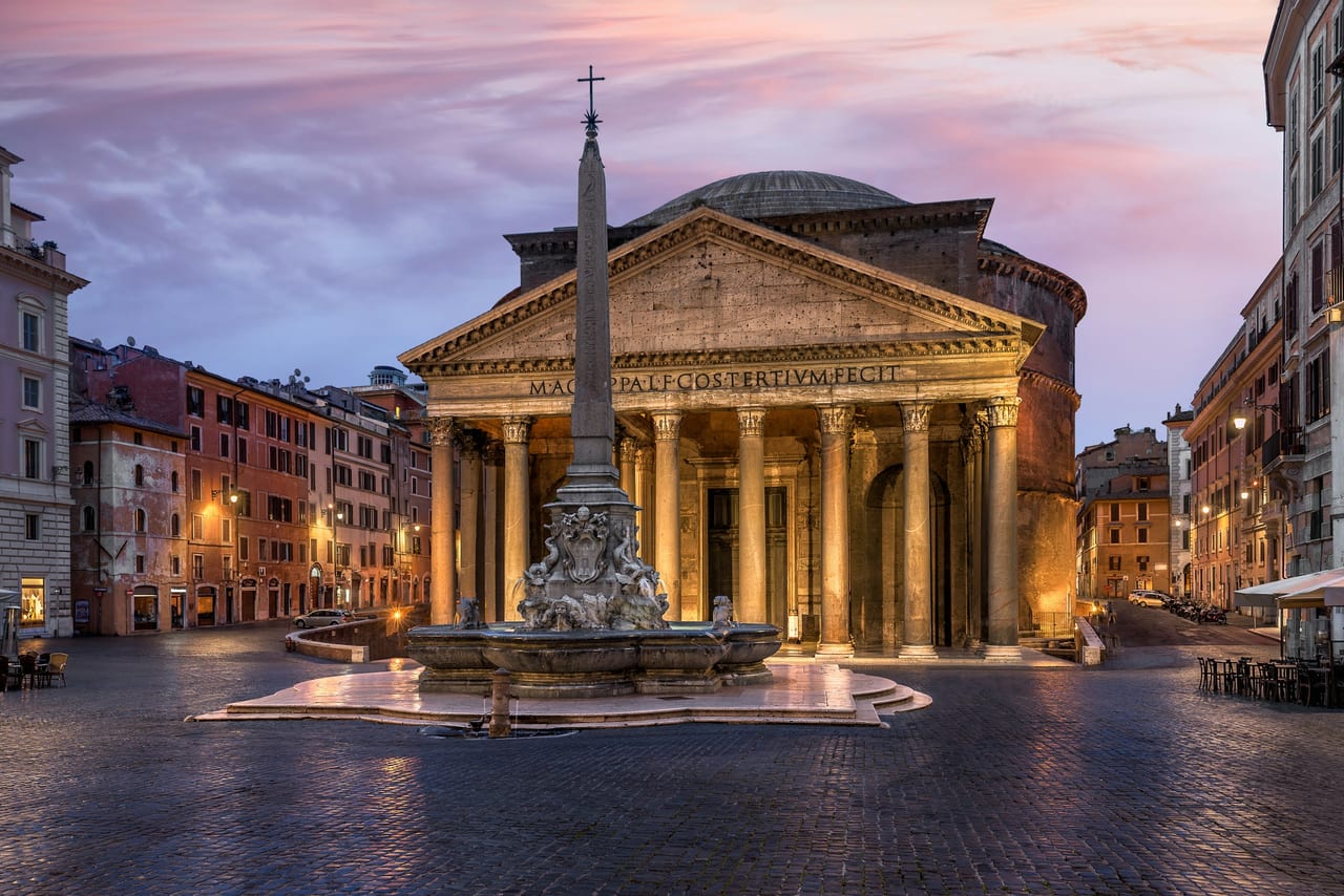 The Pantheon's granite columns and inscribed portico stand lit at dusk in Piazza della Rotonda.