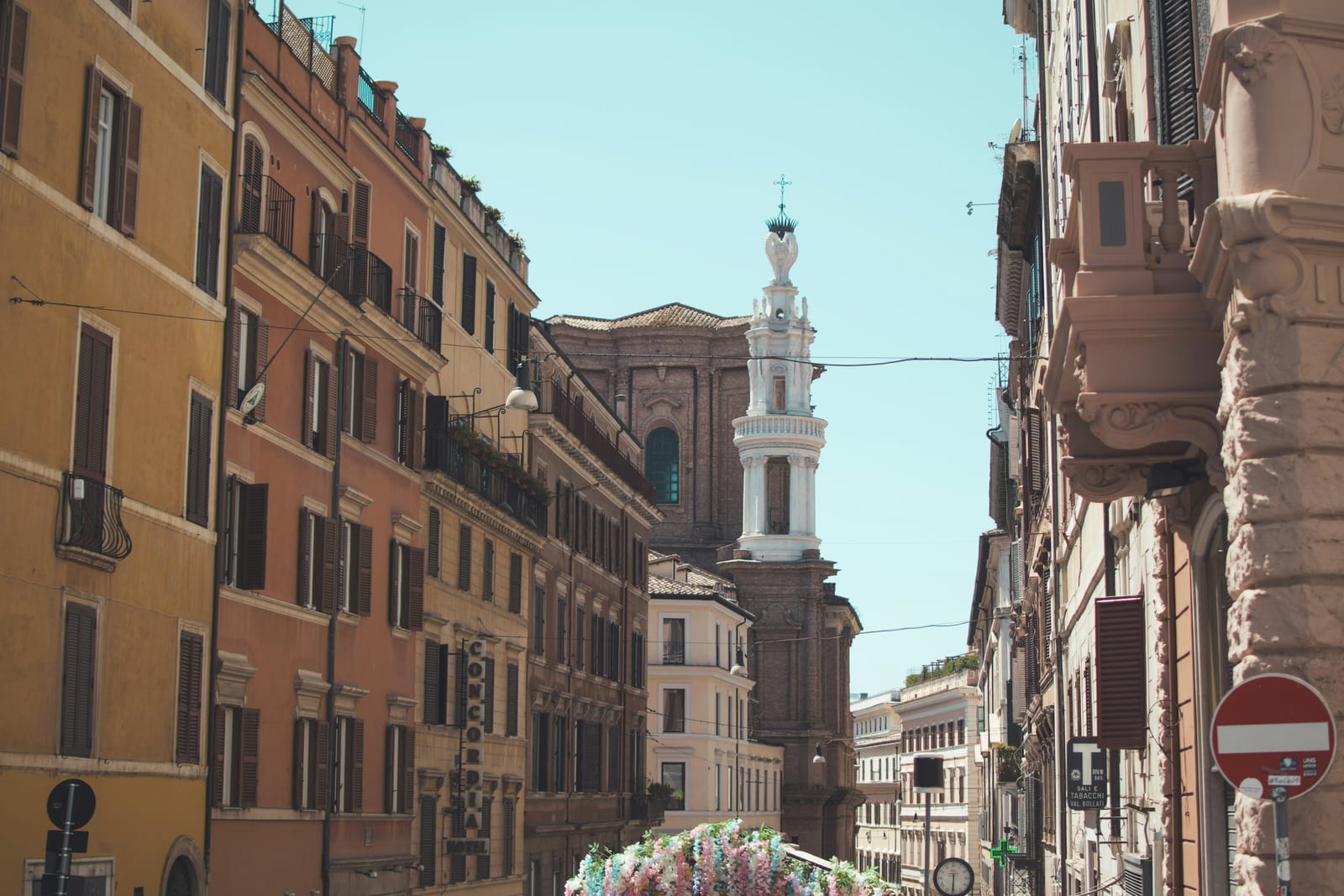 A sunlit Roman street with a church bell tower.