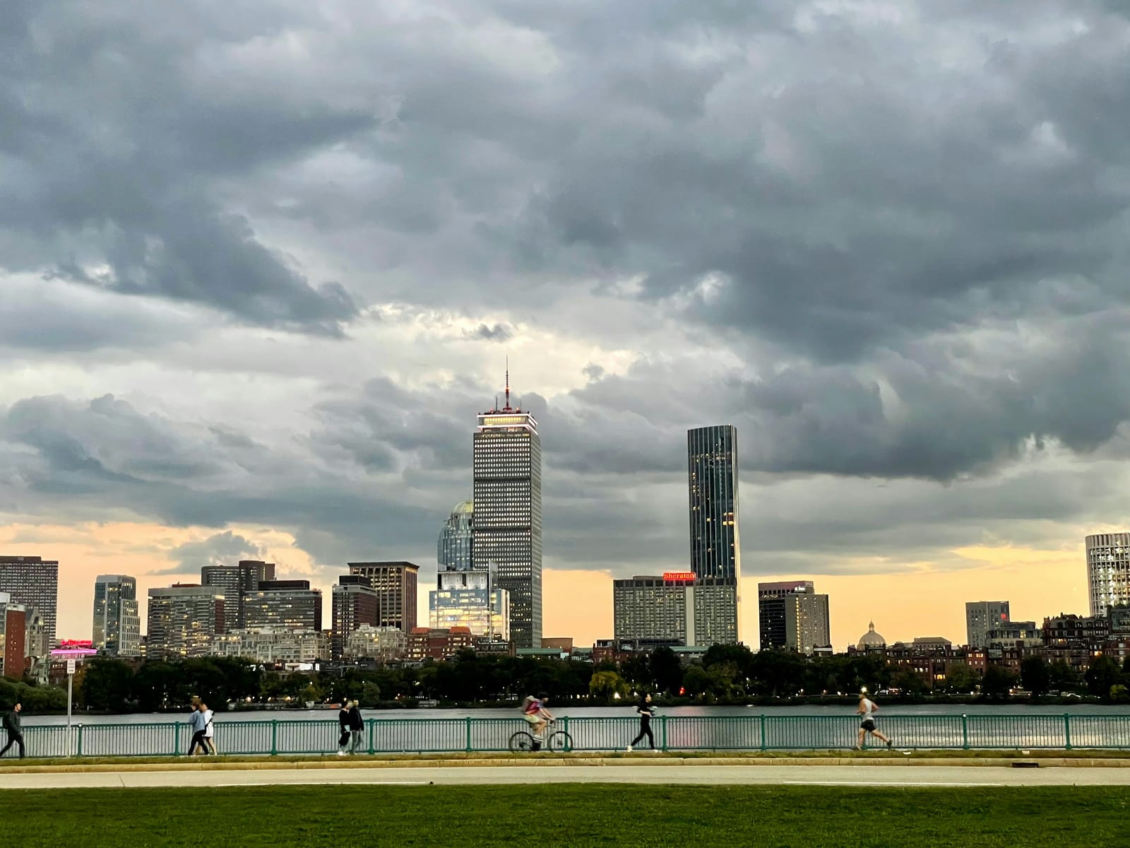 The Charles River Esplanade at dusk, its riverside path busy with walkers and cyclists beneath the Boston Back Bay skyline