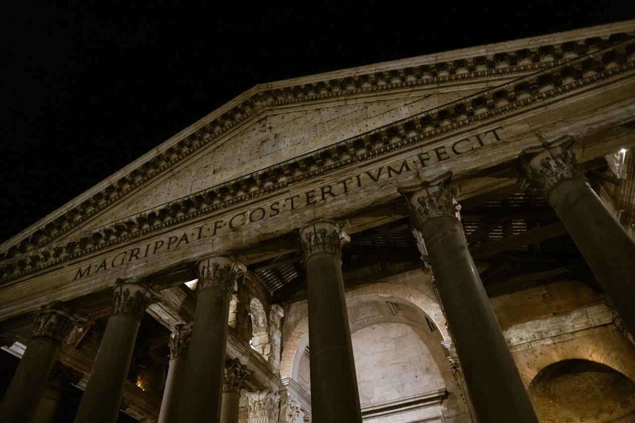 The Pantheon's granite columns and inscribed portico stand lit at dusk in Piazza della Rotonda.