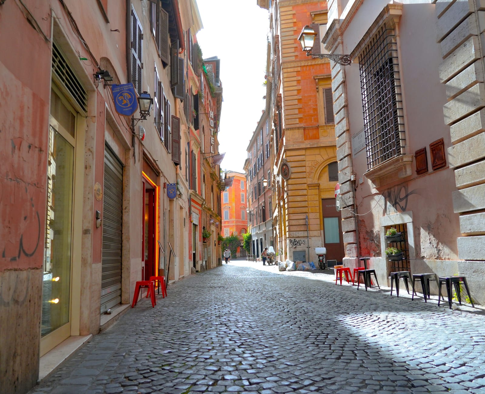 A cobblestone Monti lane with cafe stools set out along ochre buildings.